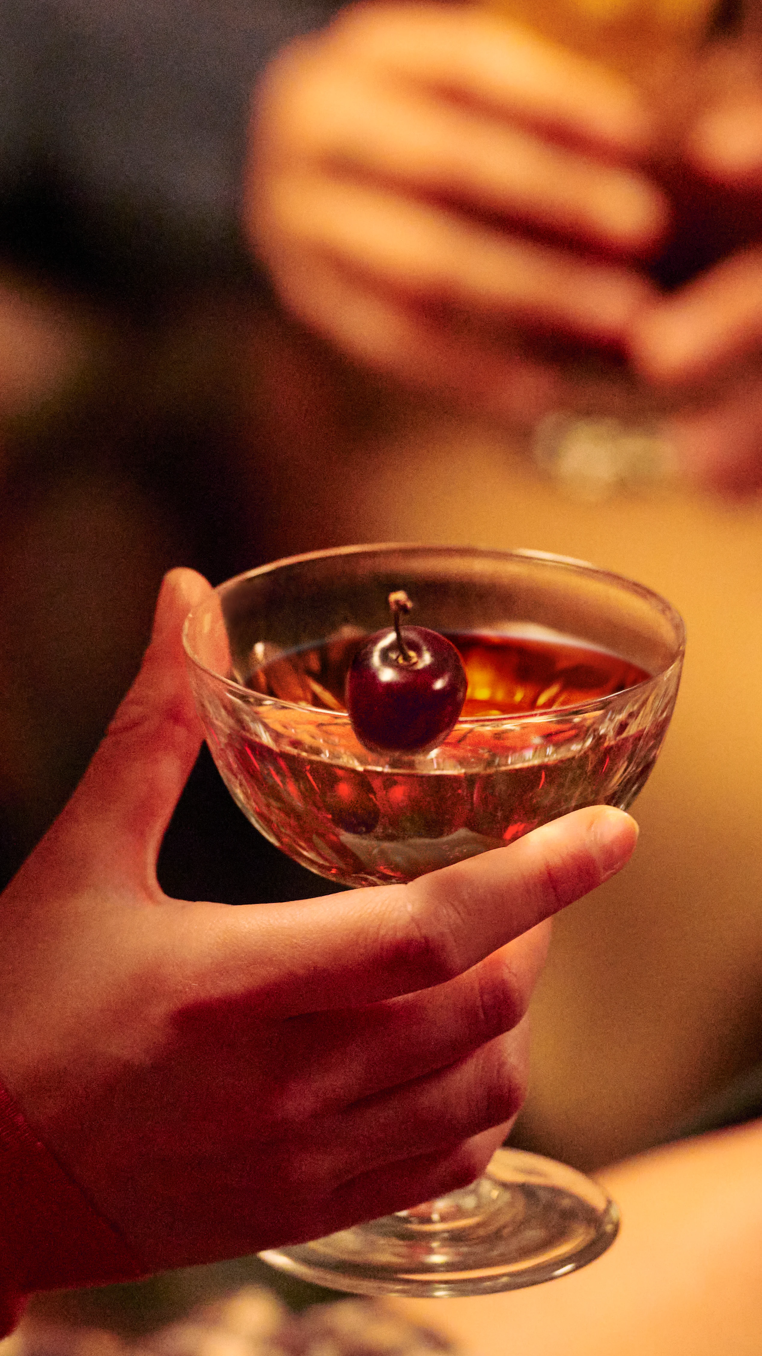 Someone holding a Manhattan cocktail in a coupe