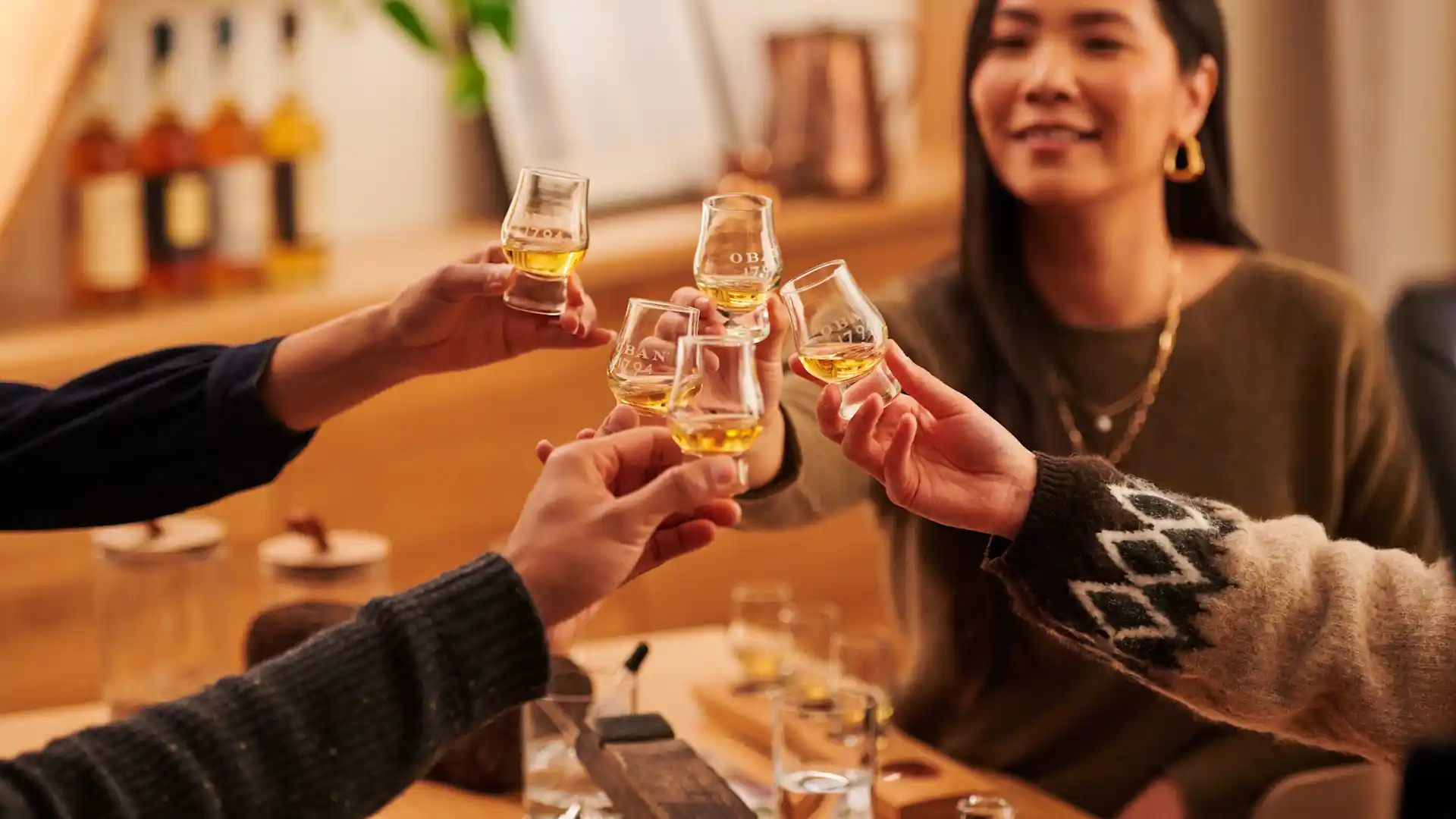 A group of friends raise tasting glasses of whisky in the air in a cheers gesture.