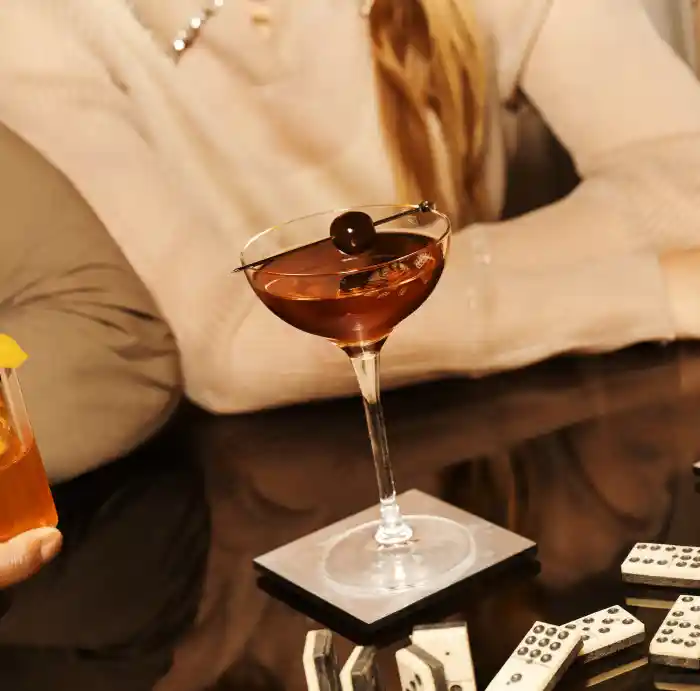 Two Old Fashioned cocktails and a Manhattan cocktail sit on a glass table