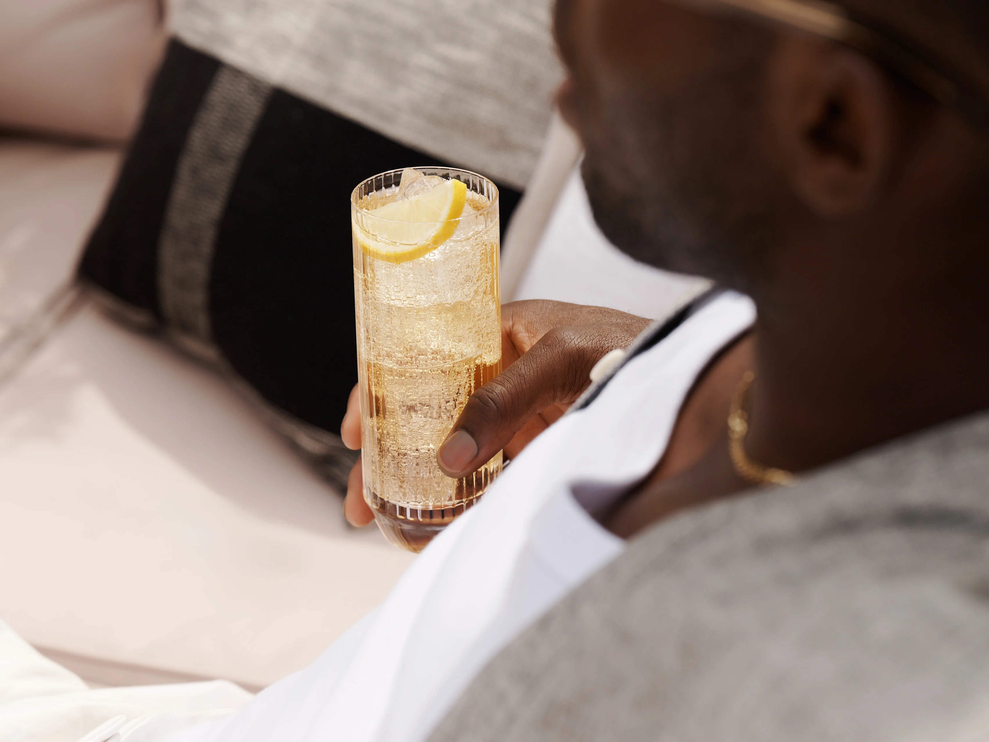 A man holds a whisky highball cocktail while sat on a sofa