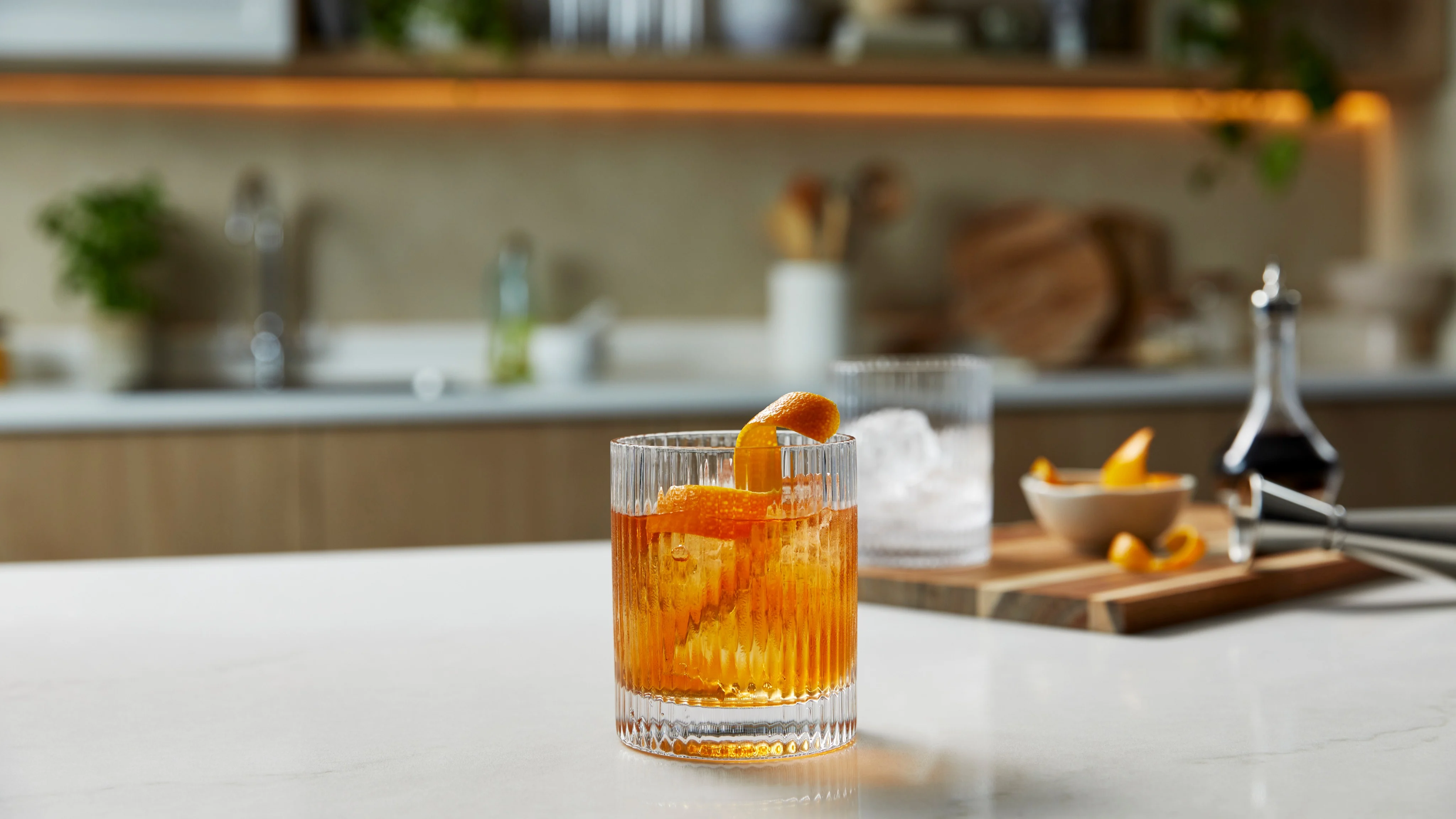 An Old Fashioned cocktail in a rocks glass, filled with ice and topped with an orange garnish.