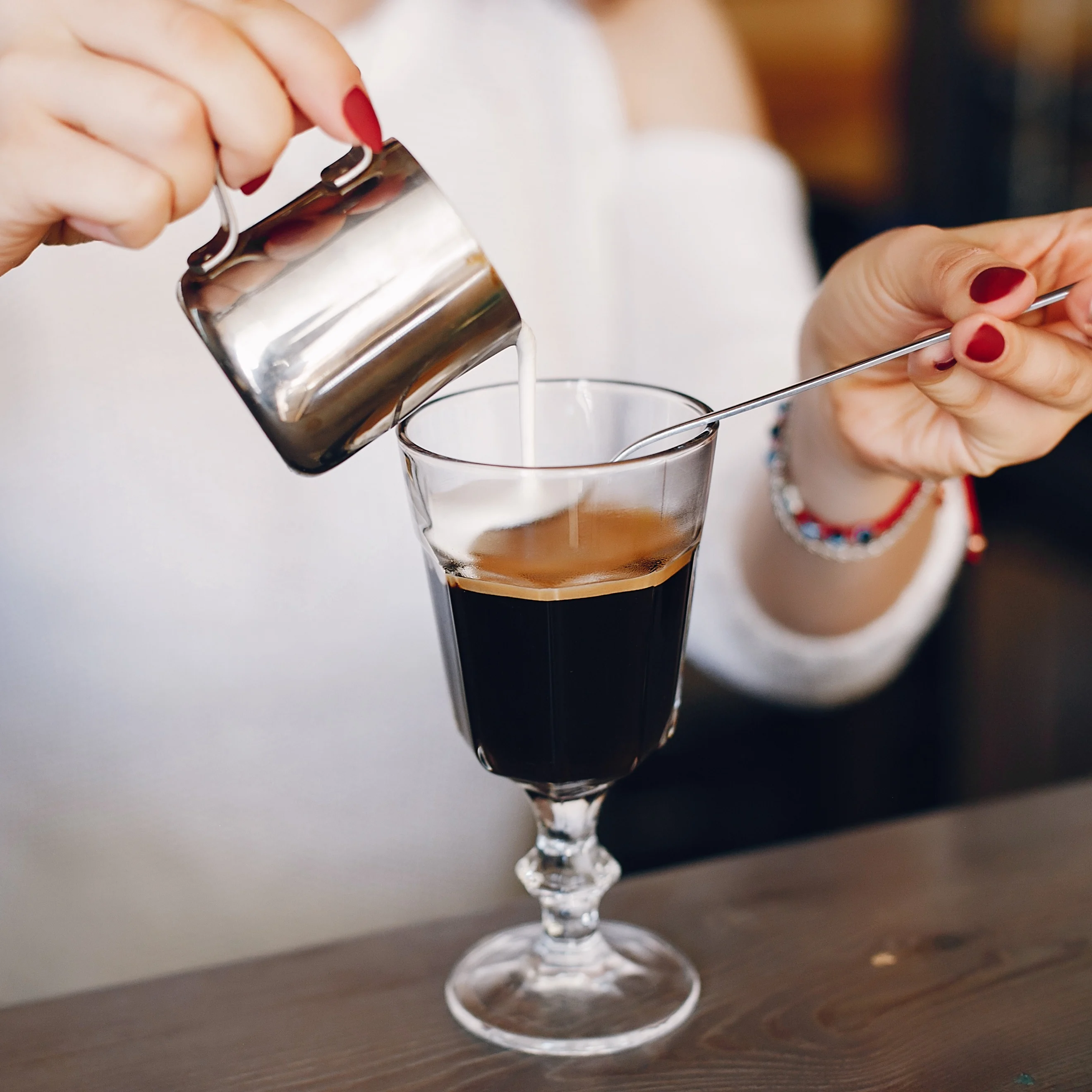 Eine Person gießt Sahne auf einen Irish-Coffee-Cocktail