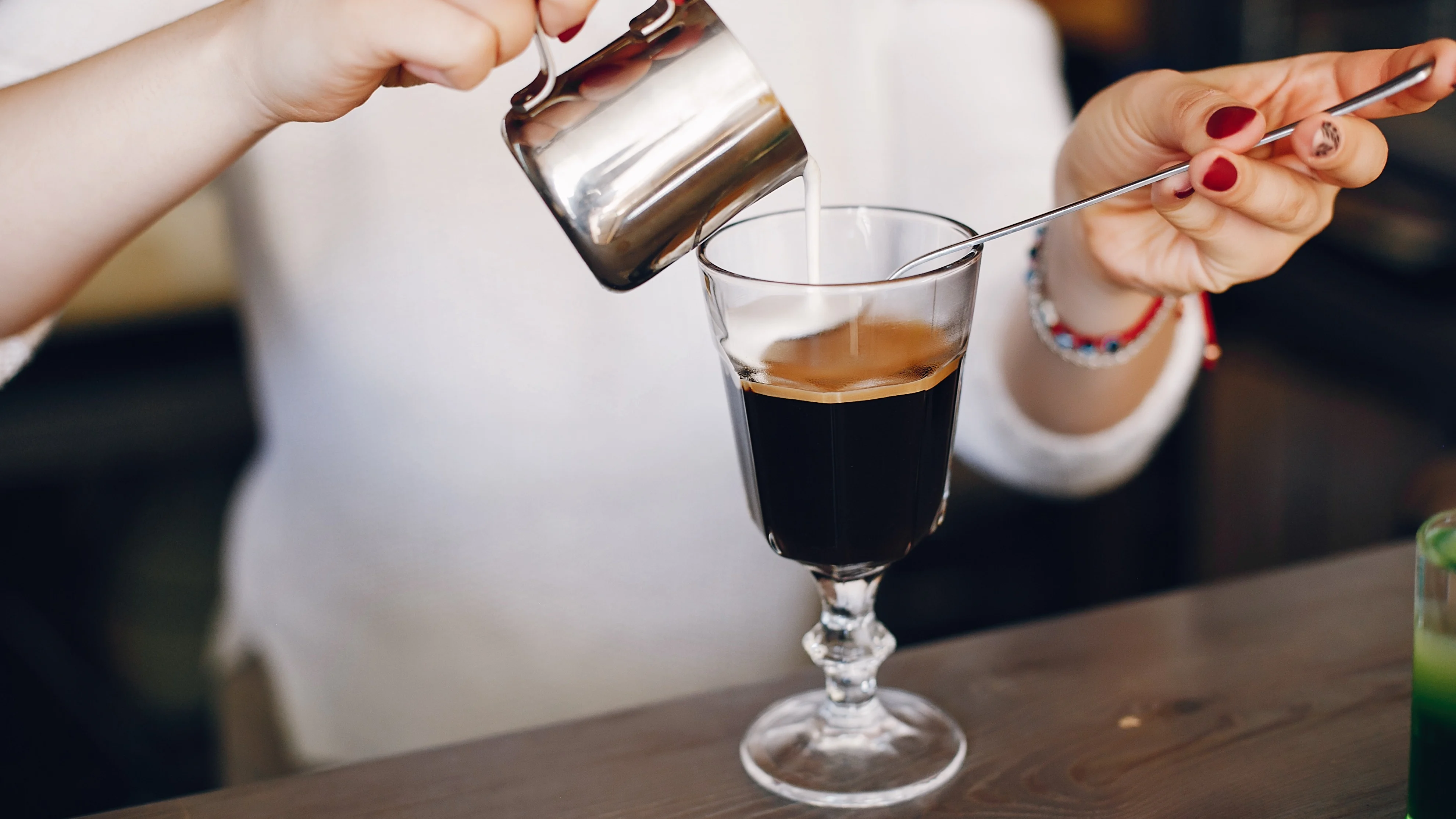 Eine Person gießt Sahne auf einen Irish-Coffee-Cocktail
