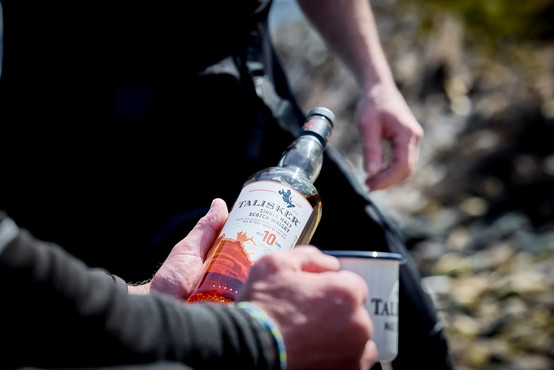 Fisherman's hands clasping bottle of Talisker Single malt scotch whisky and Talisker mug