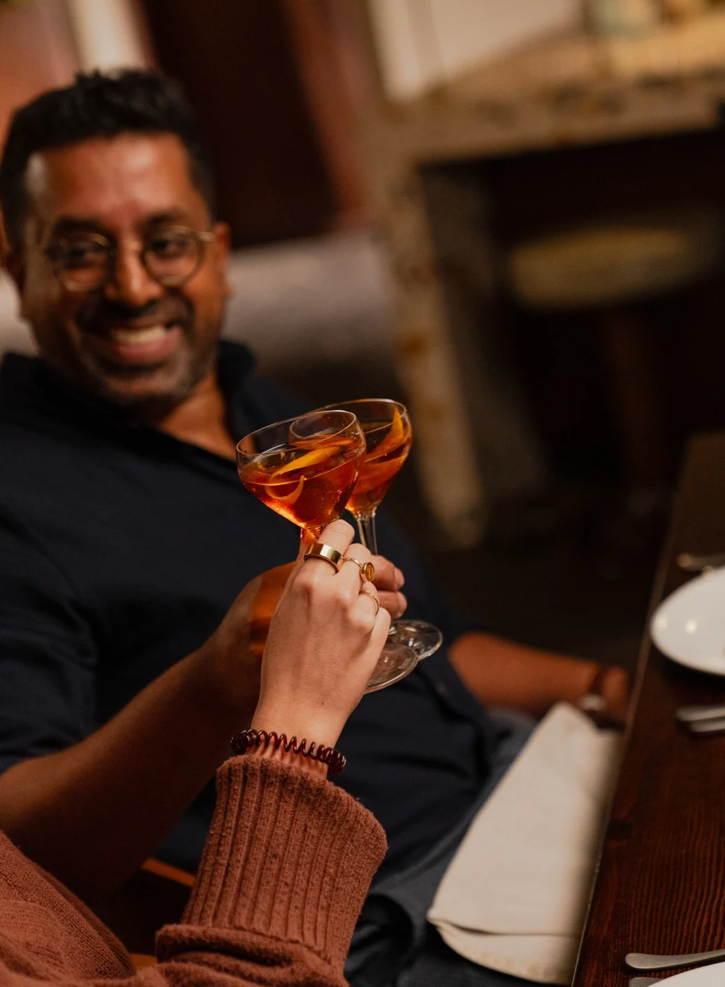 A man and a woman cheers a whisky cocktail with an orange twist. 