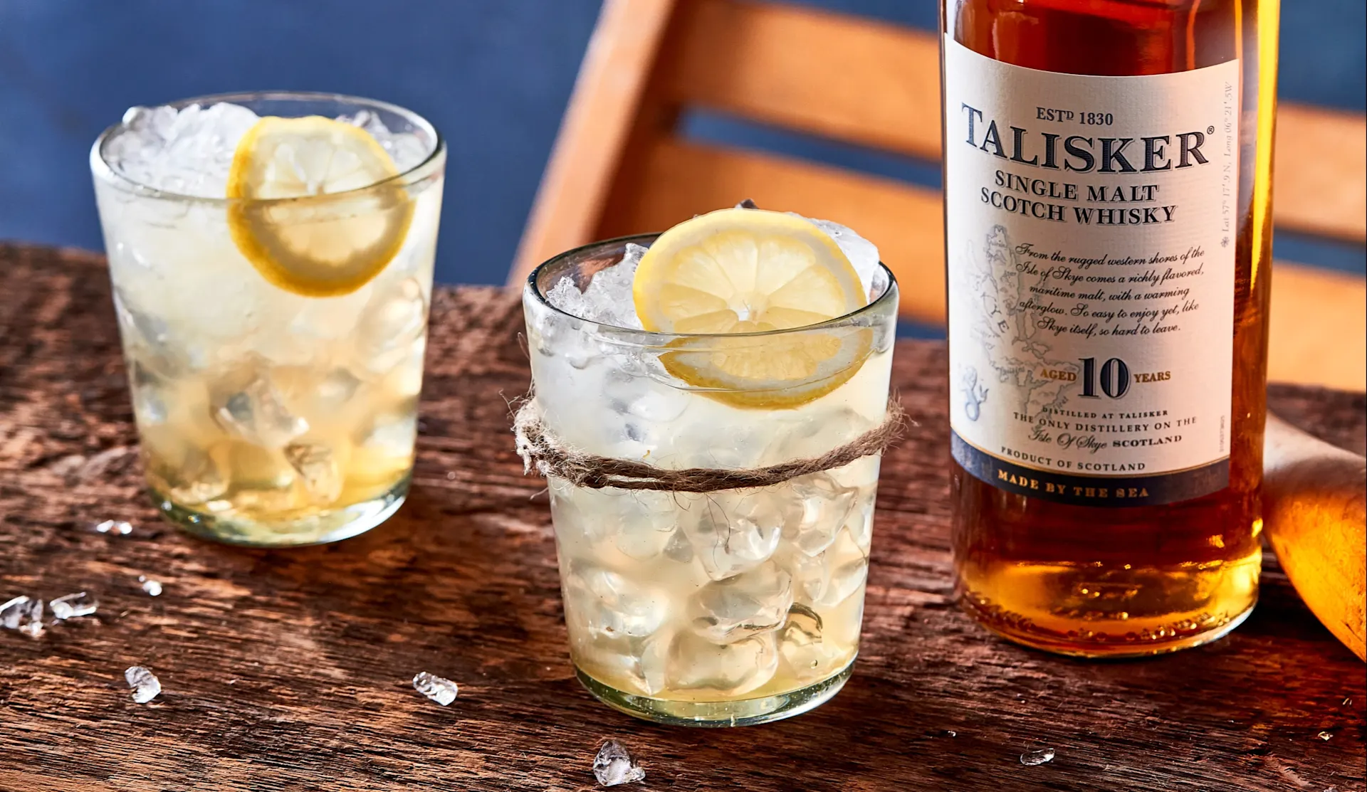 Two lowball whisky cocktails sit on a wooden board next to a bottle of Talisker 10 year old single malt whisky