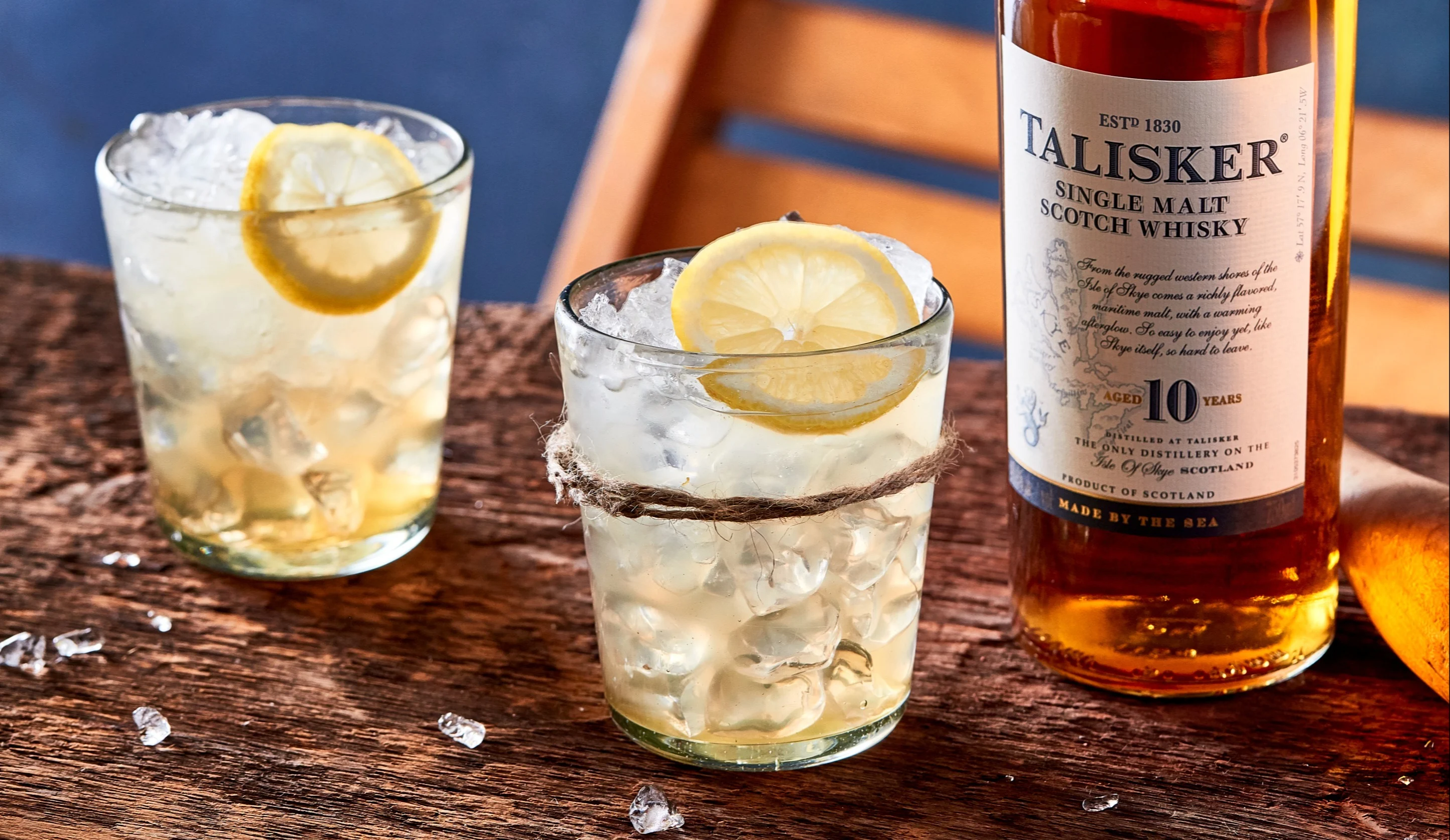 Two lowball whisky cocktails sit on a wooden board next to a bottle of Talisker 10 year old single malt whisky