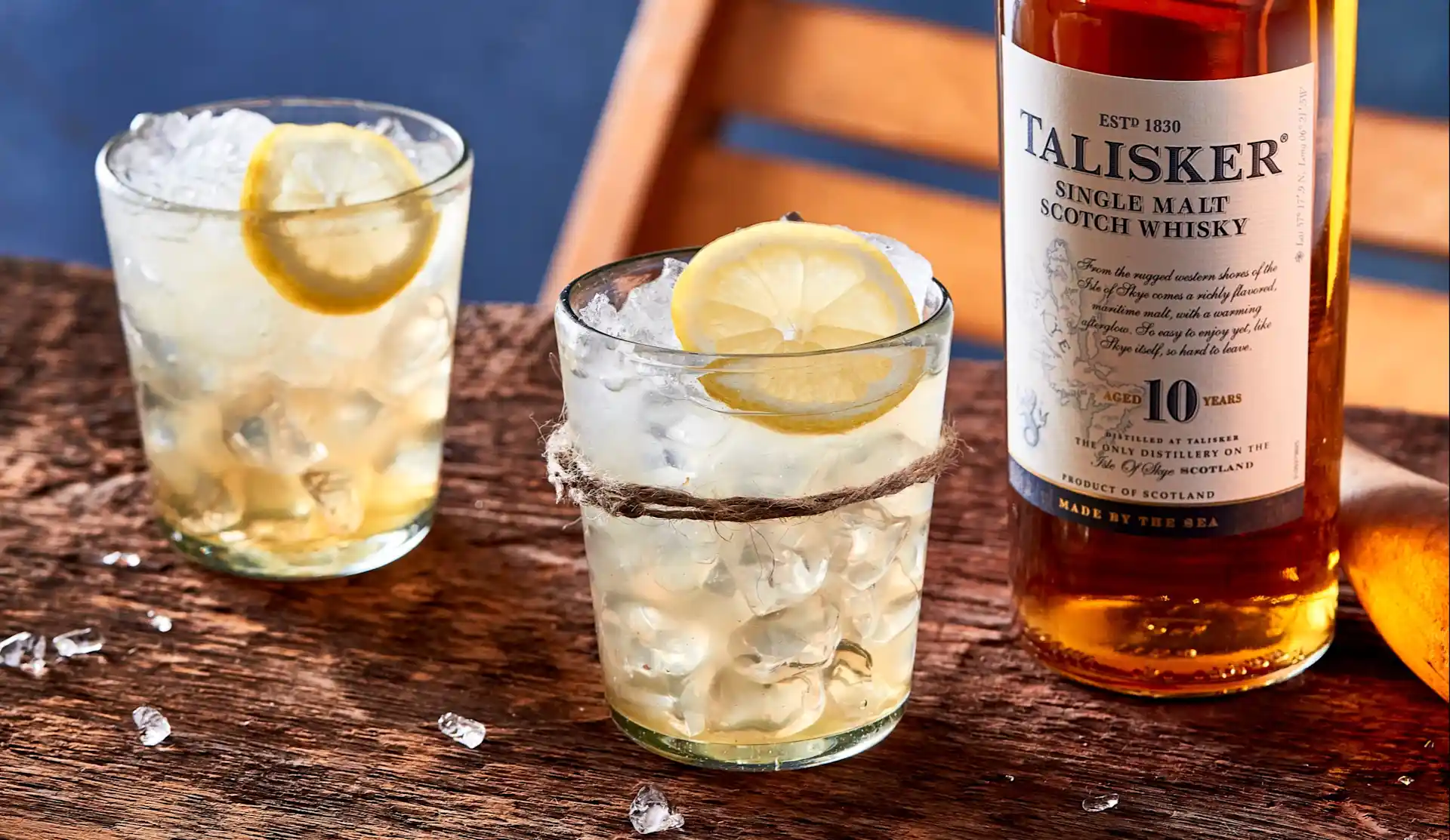 Zwei Lowball-Whisky-Cocktails liegen auf einem Holzbrett neben einer Flasche Talisker 10 Jahre Single Malt Whisky