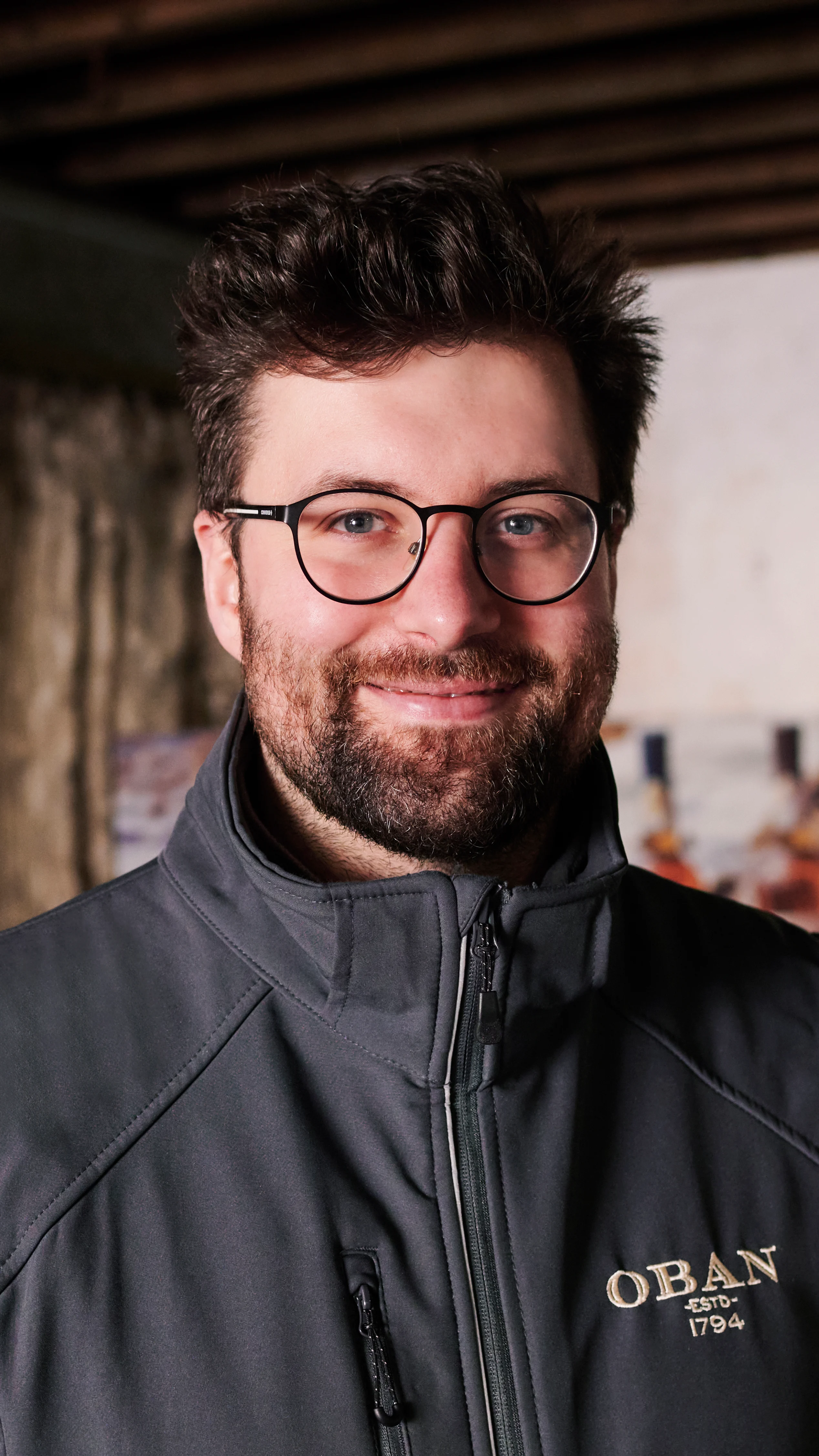 Callum, an Oban tour guide, is pictured stood in a storeroom at the distillery, wearing a grey Oban jacket.