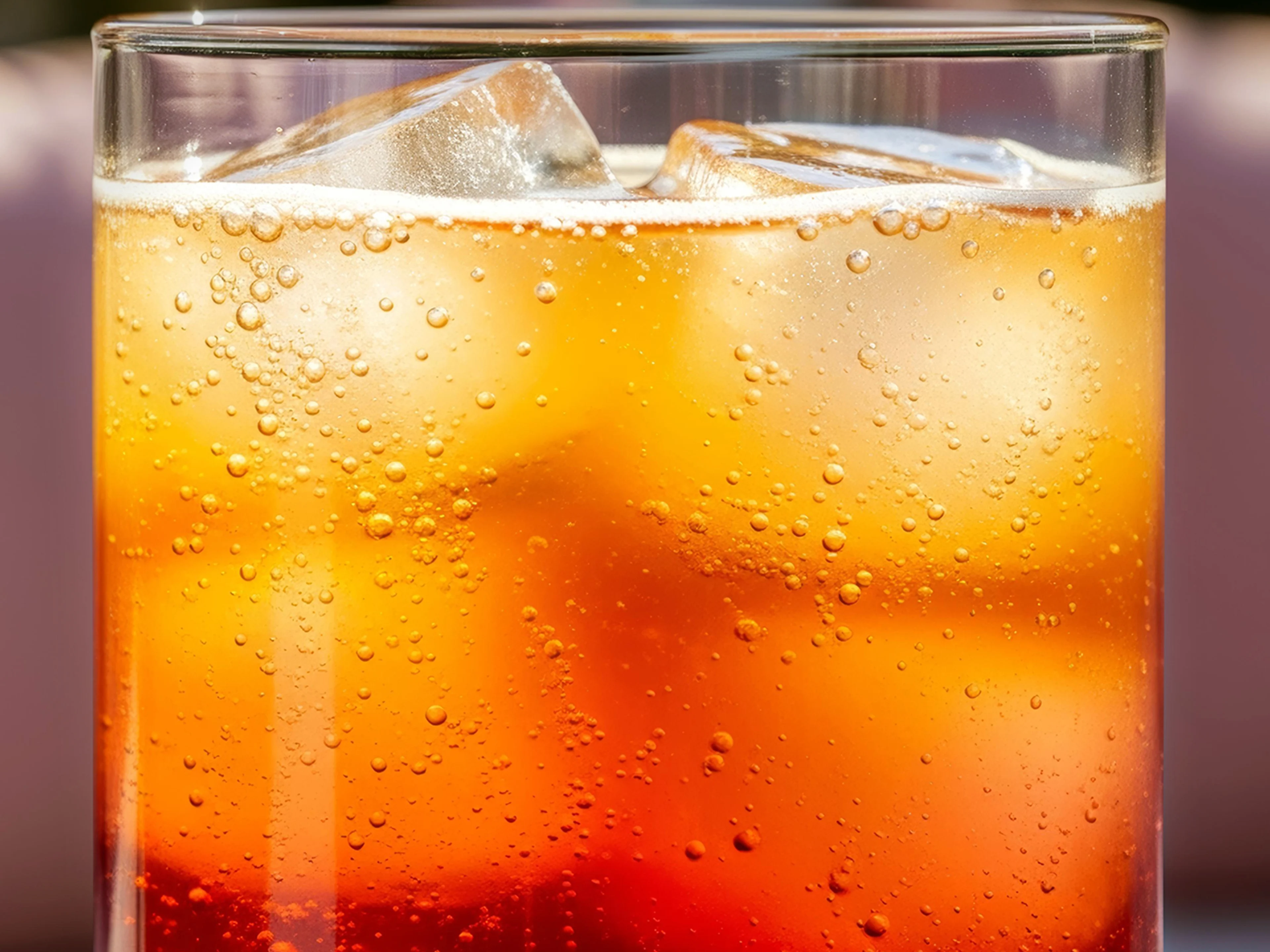 Eine Nahaufnahme einer hellbraunen Flüssigkeit in einem Highball-Glas mit Eiswürfeln und Bläschen.