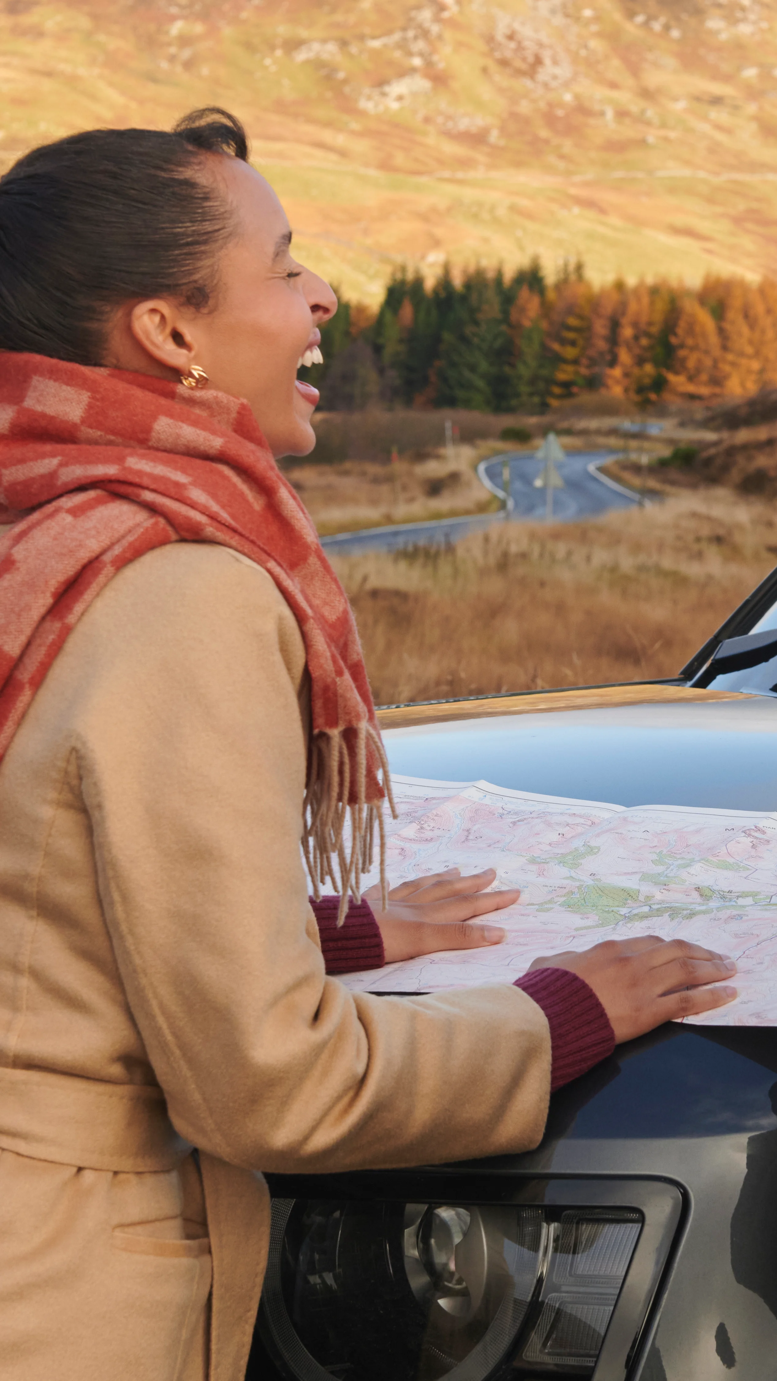 A couple consulting a map outdoors in the Scottish Highlands while planning a Highland distillery tour route, with moorland and hills stretching behind them