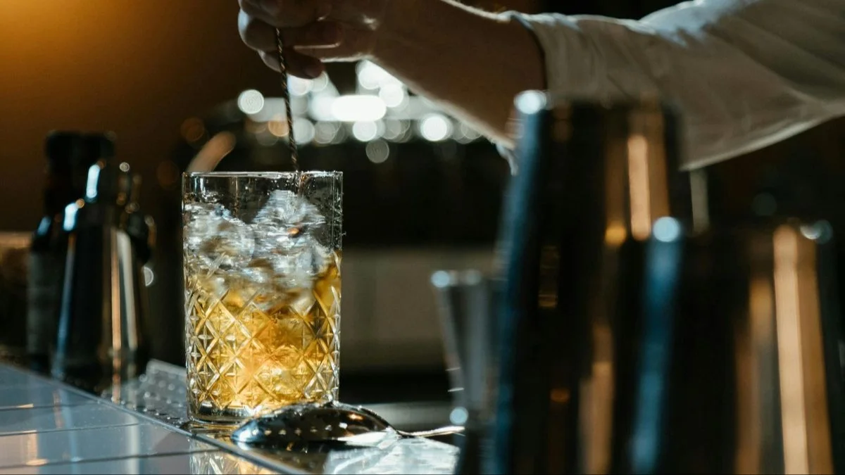 A bartender mixes a Diamondhead cocktail in a tall glass with a long spoon.