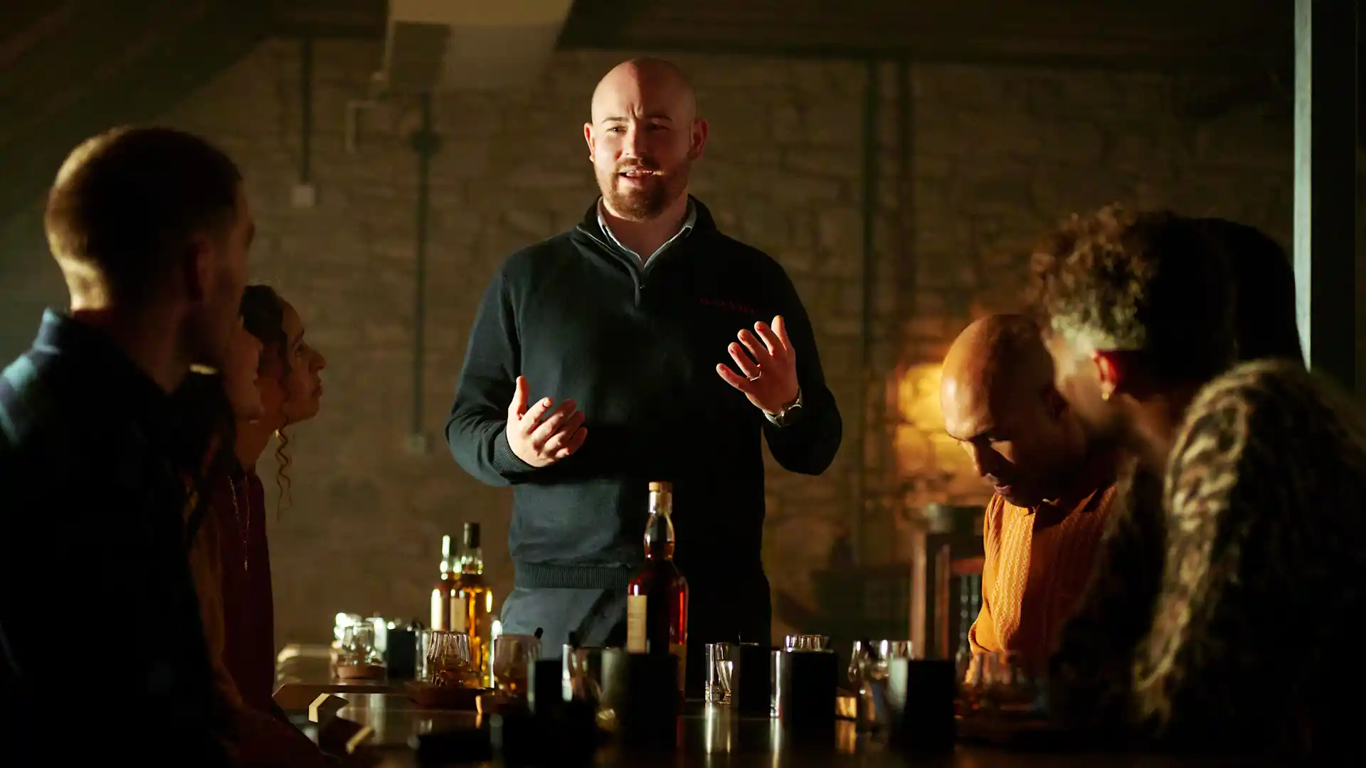 A Blair Athol tour guide leads a tasting experience for a group of friends. The friend sit at a table, with assorted bottles and glasses in front of them