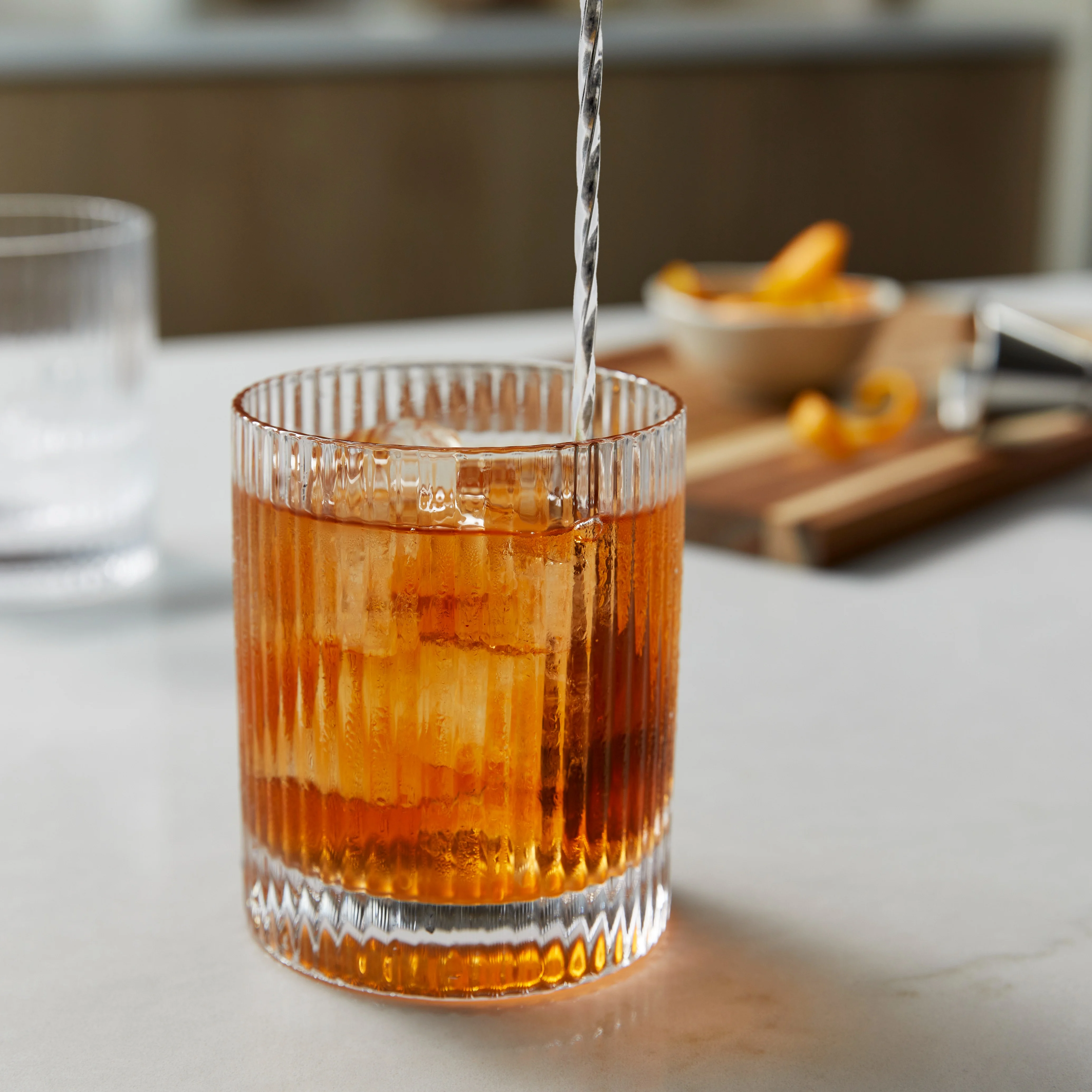 Een lichtbruin-oranje whiskycocktail in een rocksglas, die met een lange barlepel wordt geroerd
