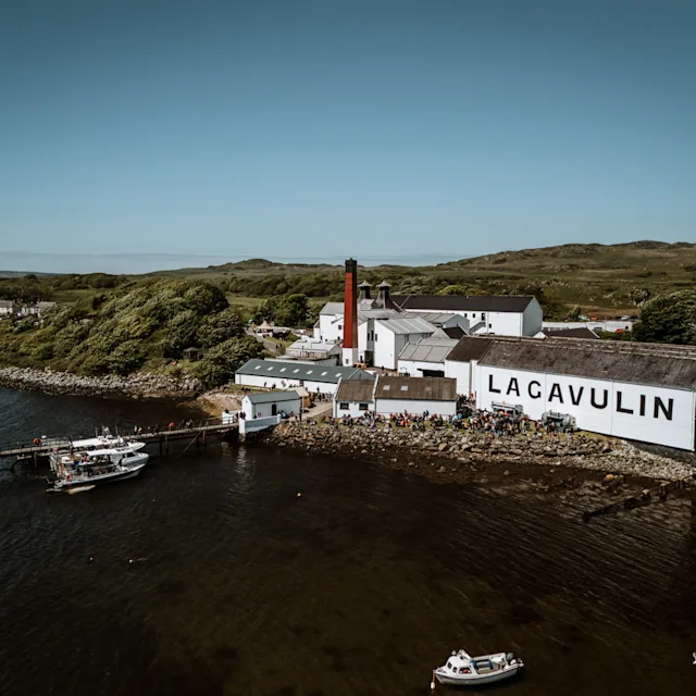 Die Lagavulin-Destillerie mit blauem Himmel und den dahinter liegenden Küsten und Hügeln.