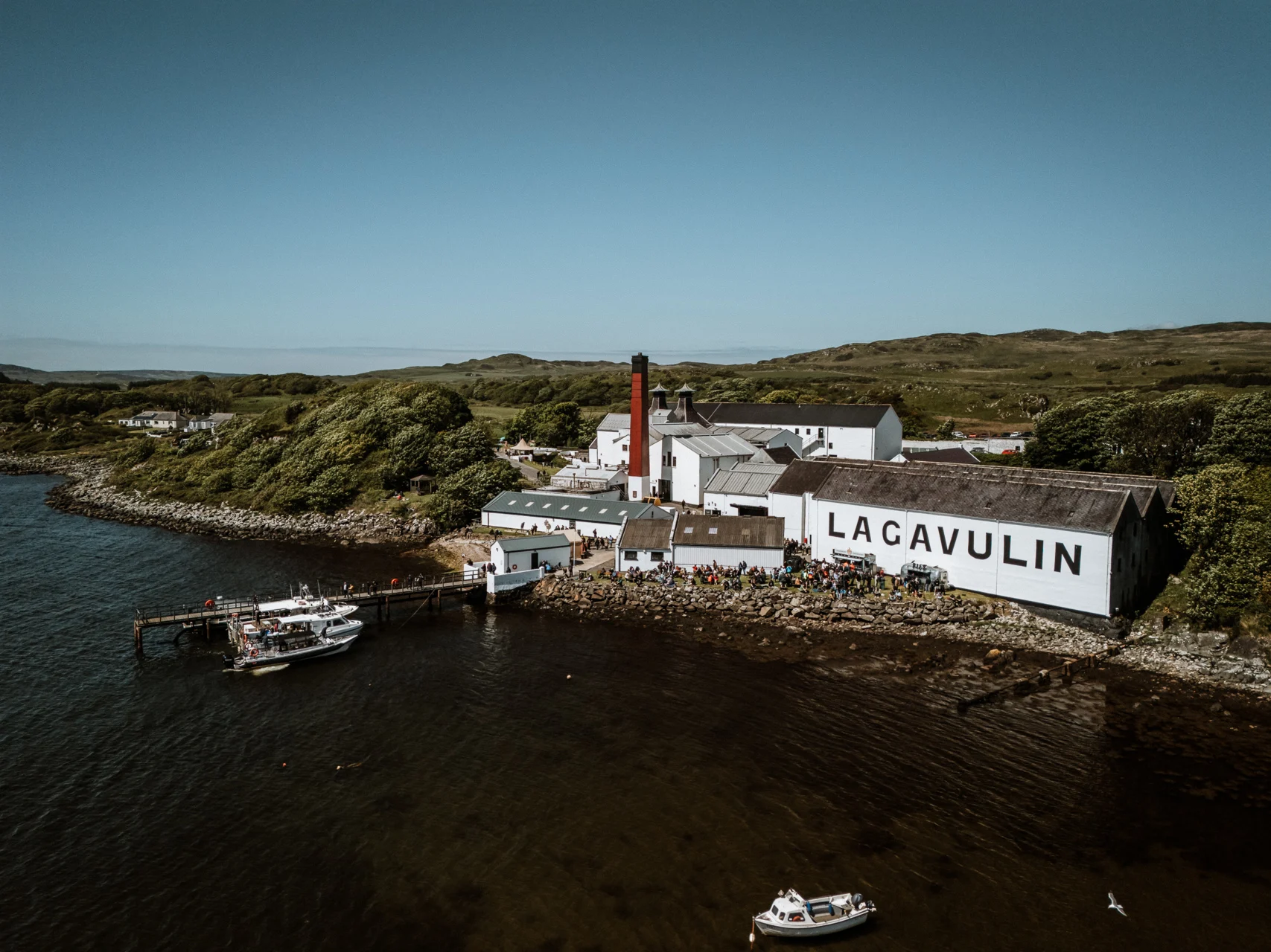 The lagavulin distillery with a blue sky and the shores and hilsd beyond.
