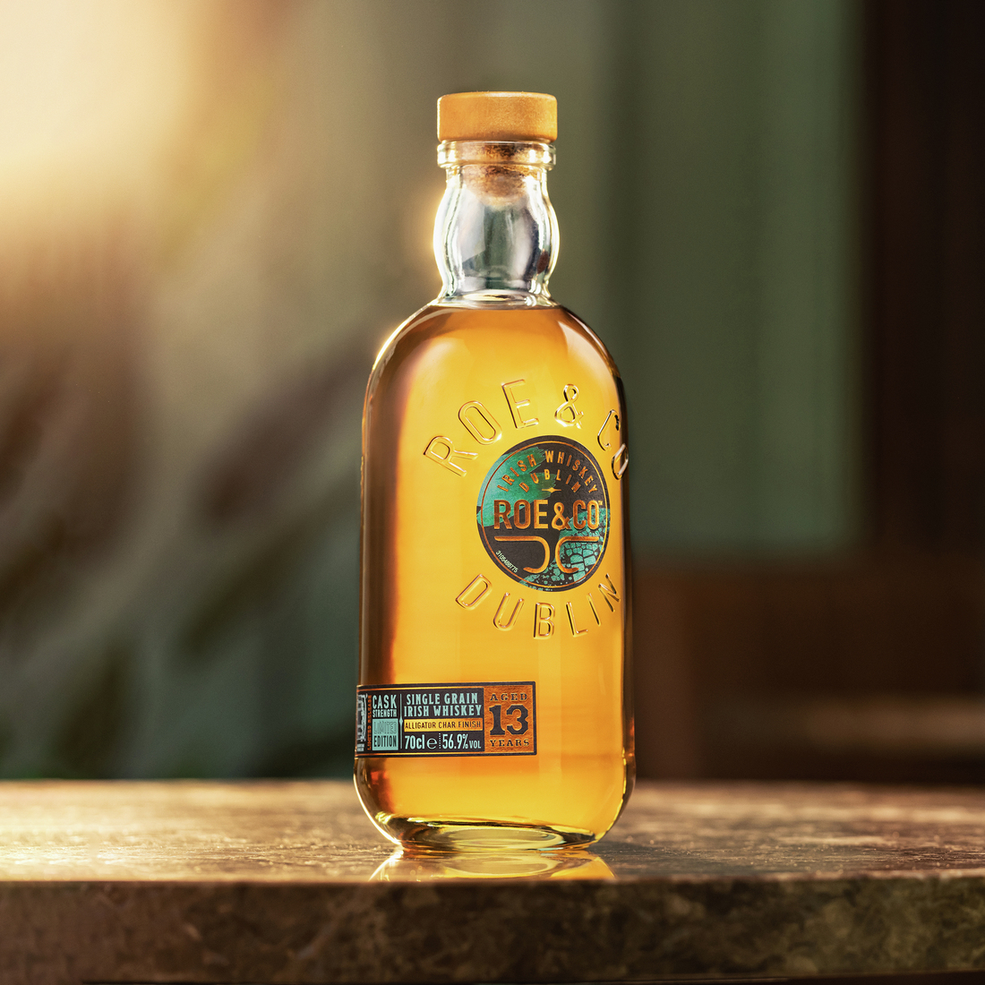 Roe & Co 13-Year-Old Cask Strength Irish Whiskey bottle standing alone on a table, bathed in soft sunlight with a blurred background.
