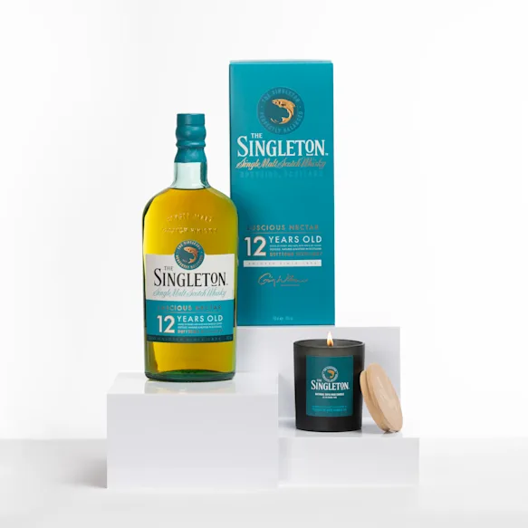 The Singleton 12-Year-Old Single Malt Scotch Whisky beside its signature candle with a wooden lid, styled on a minimalist white display.