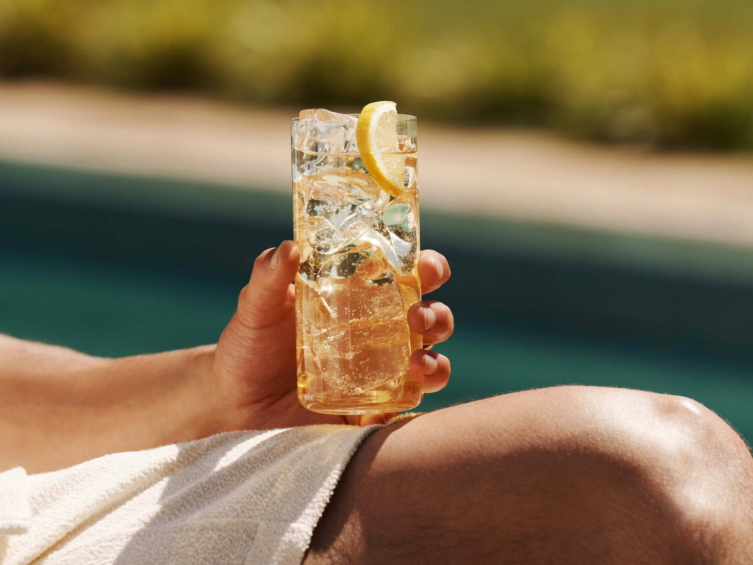 A man drinking a whisky highball cocktail by a pool