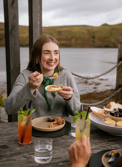 Influencer Caroline McQuistin at Talisker distillery, sitting at a wooden table outside laden with seafood and whisky cocktails