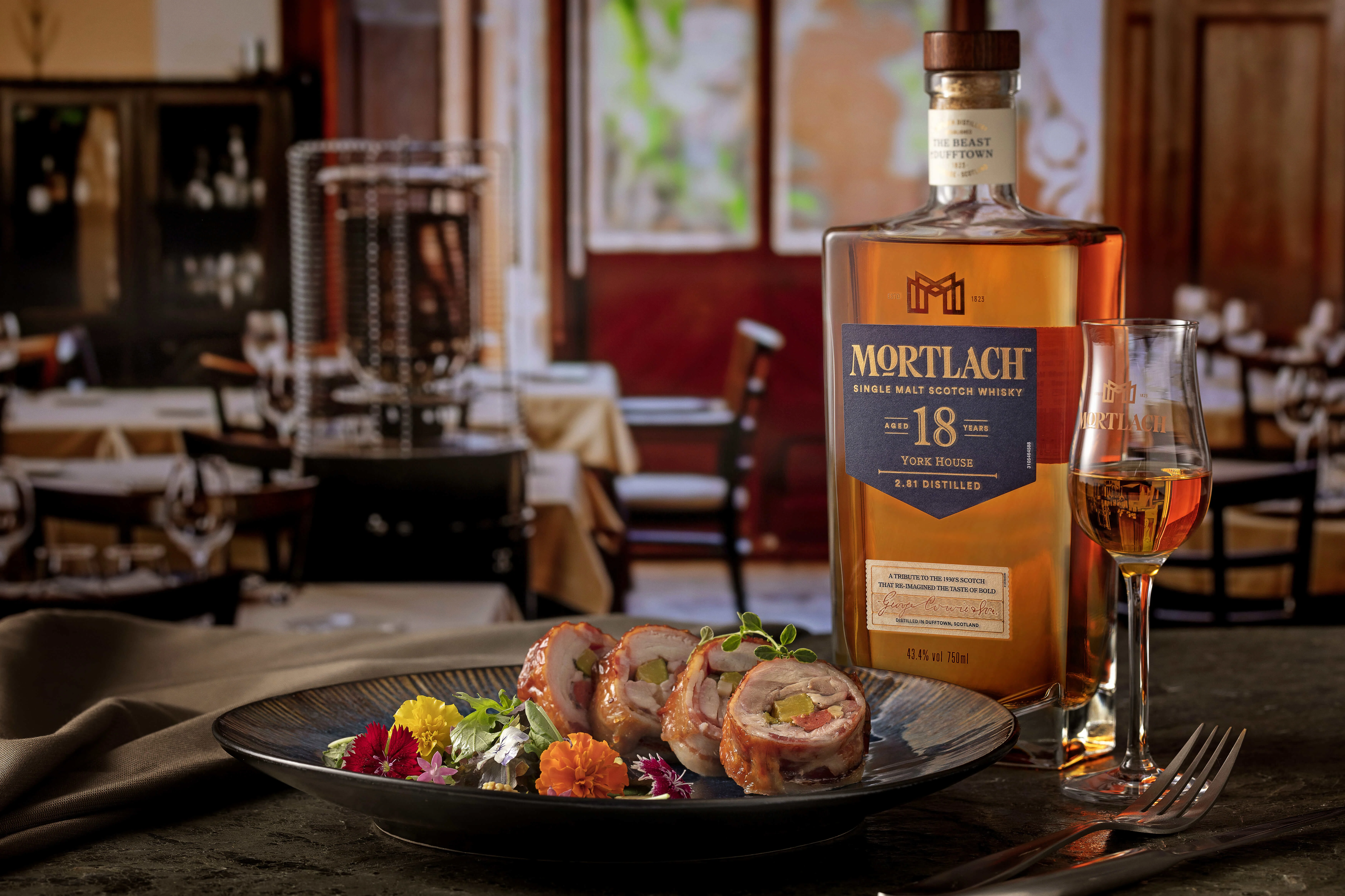 一瓶18年陸羽威士忌、一杯威士忌，以及一盤切片的精緻雞肉料理，擺放在一張配有餐具的桌子上。