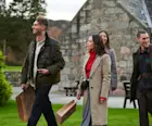 A group of friends leave Royal Lochnagar distillery, walking away from the building and carrying gift bags. They are all smiling.