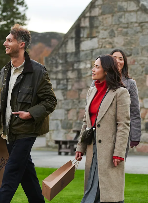 一群朋友離開 Royal Lochnagar 酒廠,拎著禮物袋離開建築物。他們都面帶微笑。