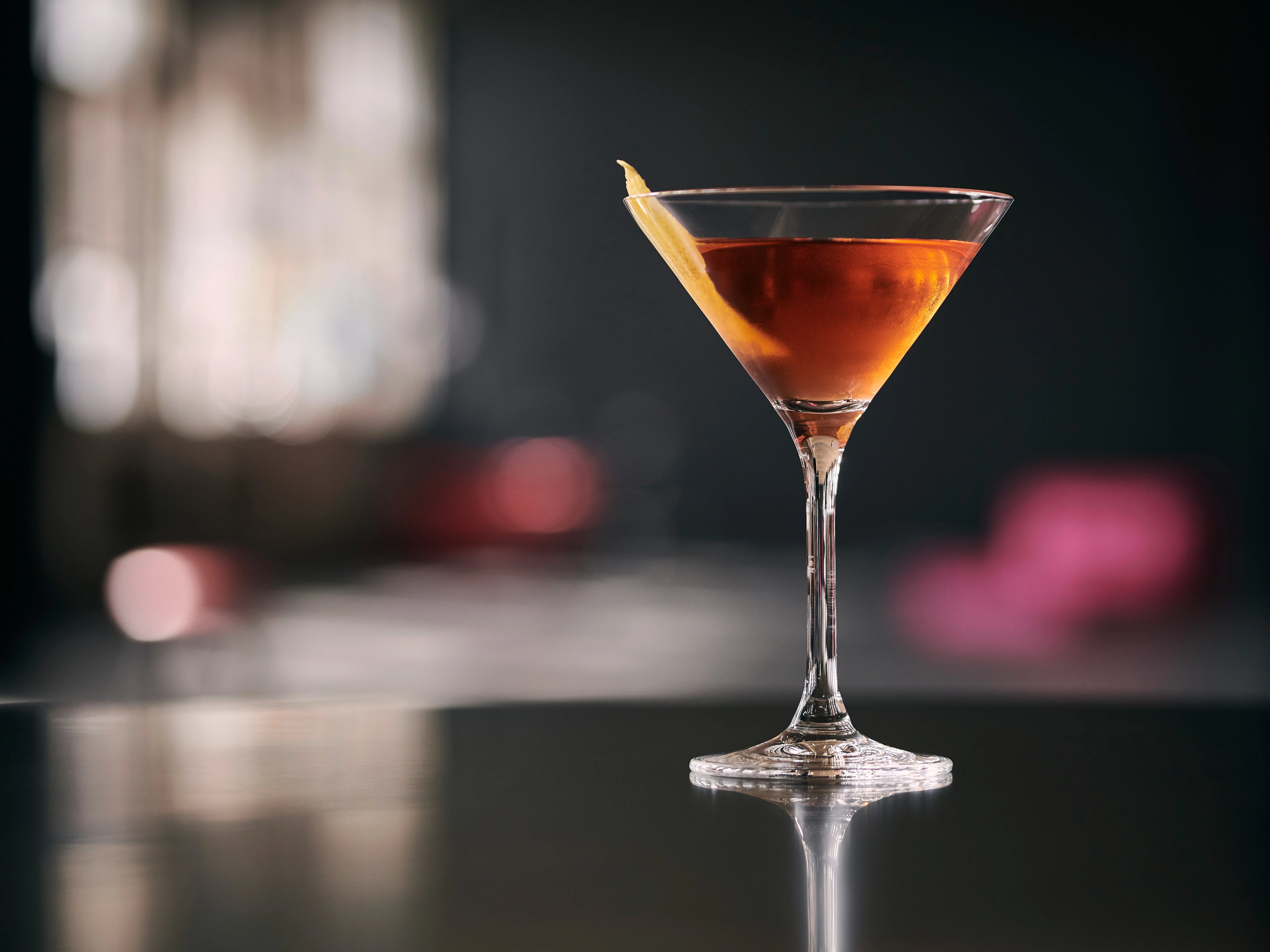 Ein braun-orangefarbener Cocktail in einem Martiniglas mit einer gedrehten Orangenschale als Garnitur