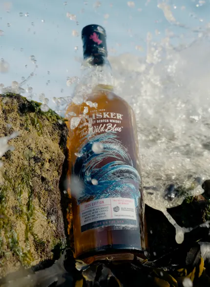 Talisker The Wild Blue whiskyfles geplaatst op een rots met oceaangolven die eromheen klotsen