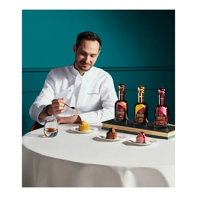 Chef Nicolas Rouzaud seated at a table, carefully plating a dessert alongside The Singleton Gourmand Collection bottles, desserts, and a glass of whiskey.