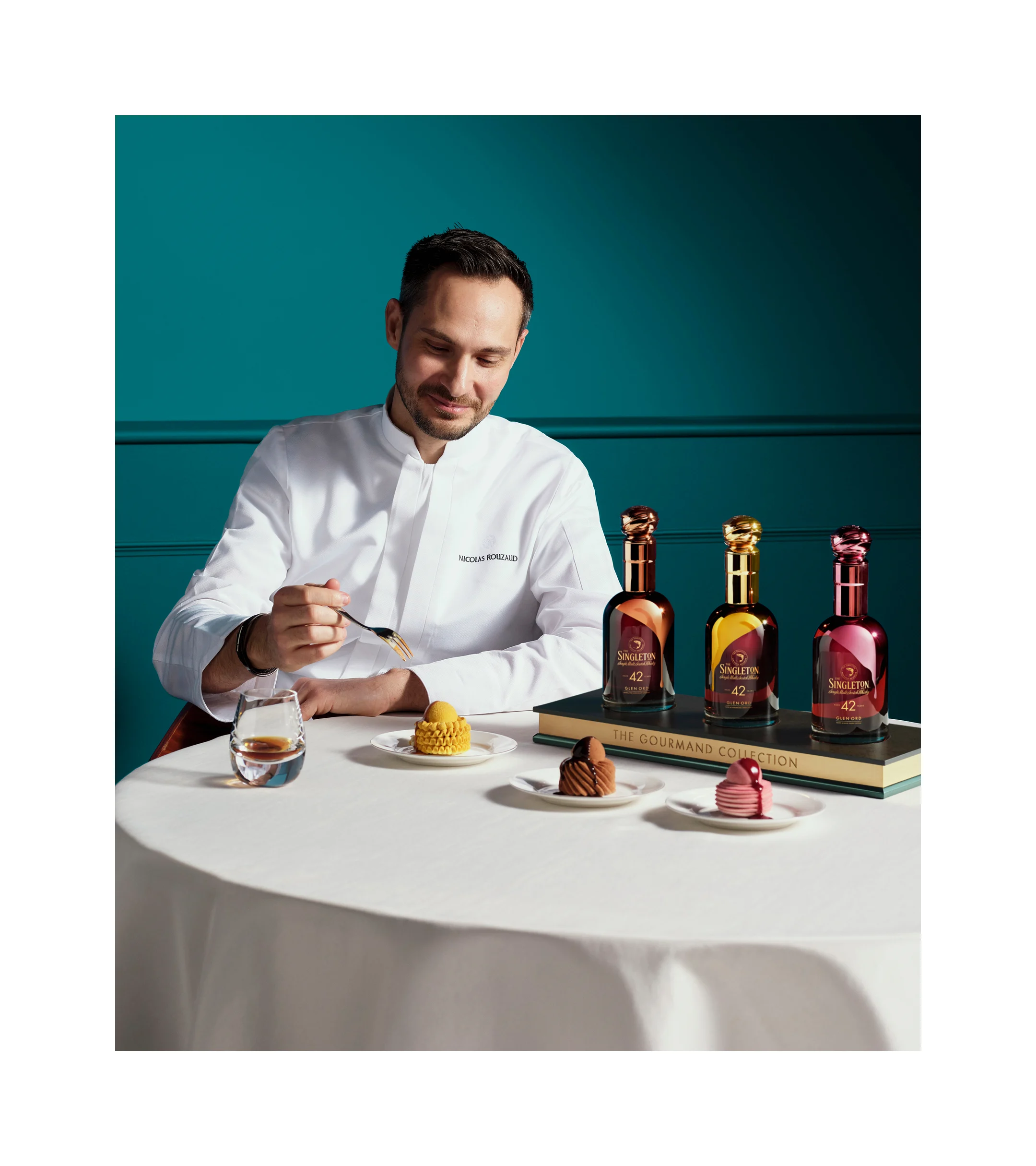 Chef-kok Nicolas Rouzaud zit aan tafel en serveert zorgvuldig een dessert naast flessen uit de Singleton Gourmand Collection, desserts en een glas whisky.