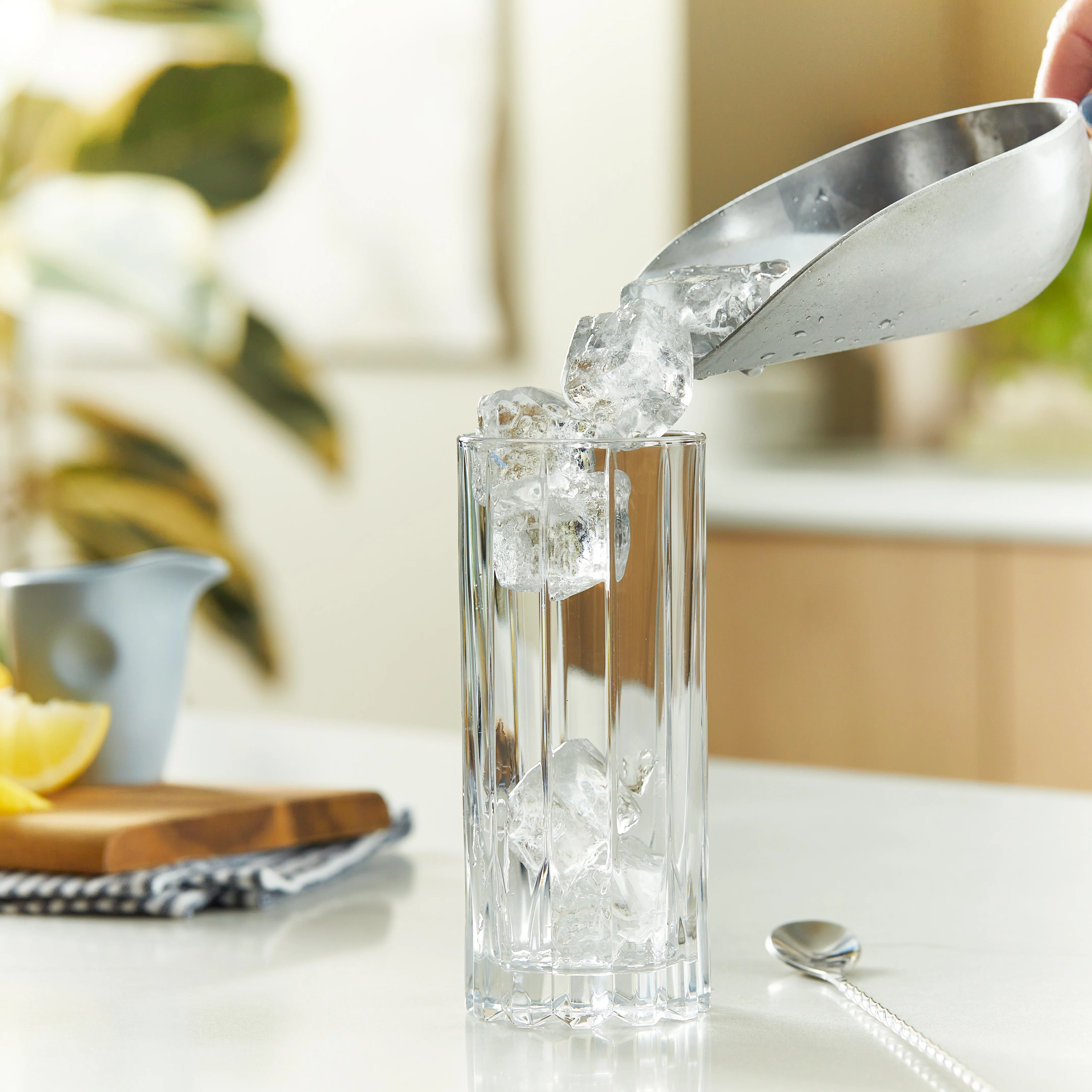 Ein silberner Barlöffel gießt Eis in ein Highball-Glas auf einem Küchentresen.
