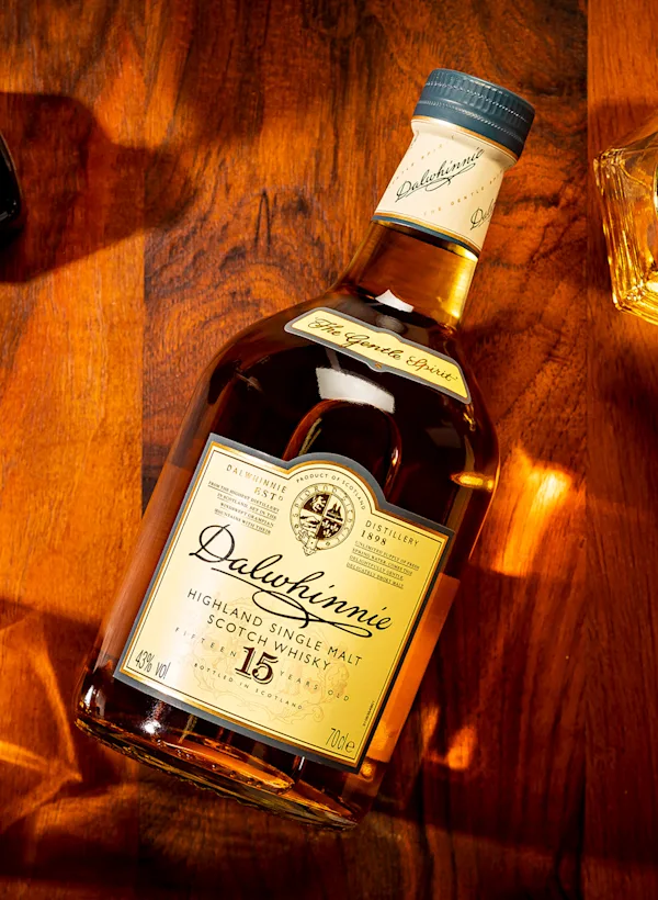 Eine Flasche Dalwhinnie-Whisky liegt mit dem Etikett nach oben auf einer Holzfläche. Um die Flasche herum stehen verschiedene Steingläser und ein Tintenfass mit Federkiel