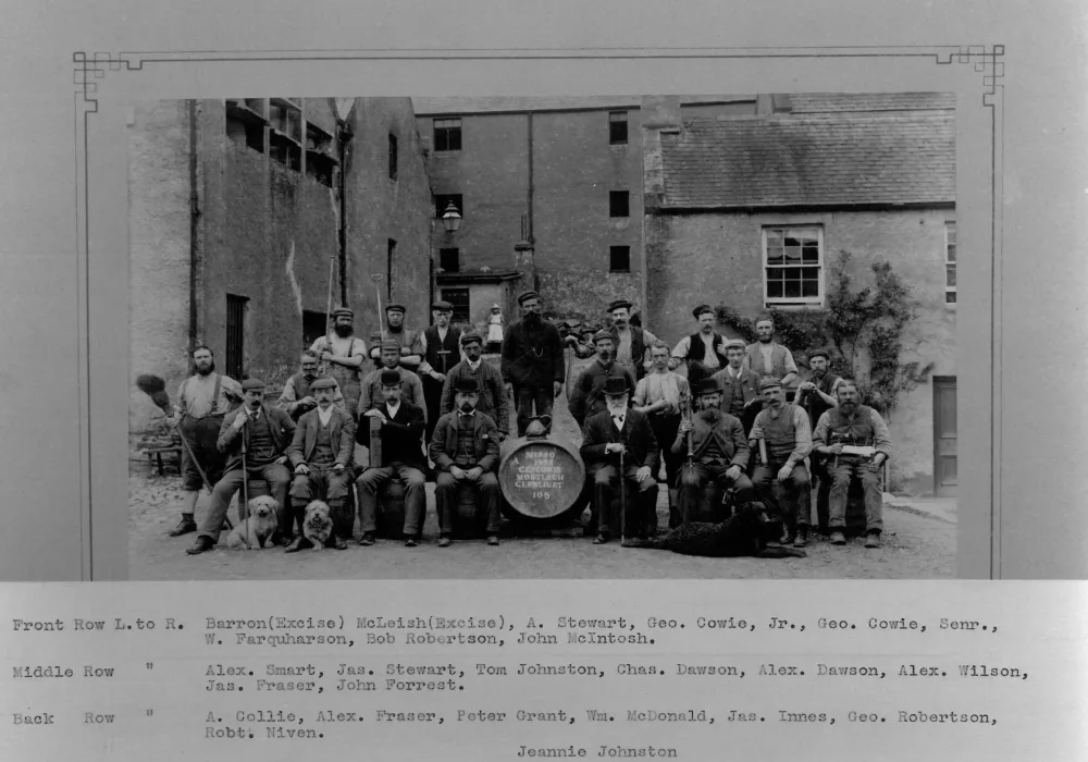 Een zwart-witfoto van verschillende mannen in Victoriaanse kleding. De voorste rij mannen zit en in het midden staat een houten ton. Achter de zittende mannen staan mannen. Achter de groep staan gebouwen.