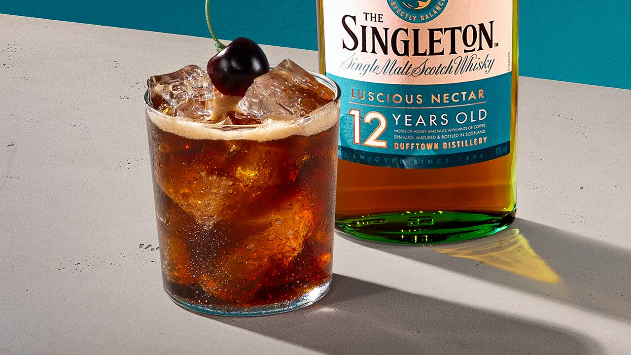 Ein Whisky-Cocktail mit einer Kirsche oben drauf neben einer Flasche The Singleton 12 Jahre Single Malt Scotch Whisky.