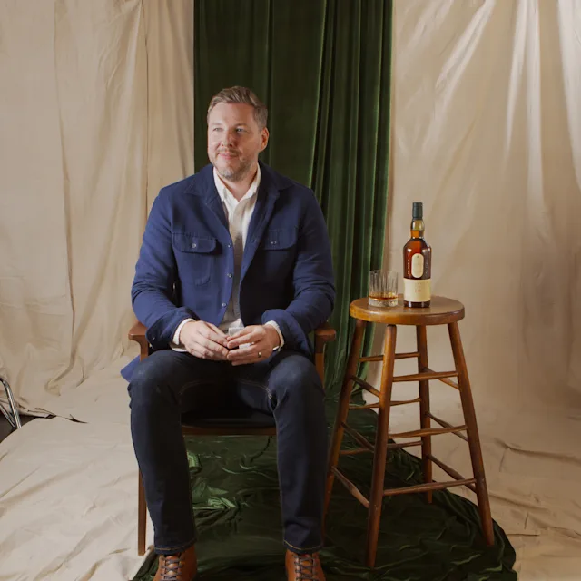 Explore More Greg King smiles as he sits beside a bottle of Lagavulin 16 Year and a rocks glass.