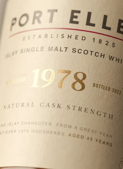 A bottle of Port Ellen whisky lies label-up on a neutral backdrop.