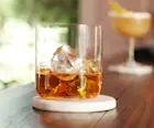 Auf der Bar steht ein Eisglas mit Whisky und Eis, dahinter ein Cocktailshaker und ein Jigger.