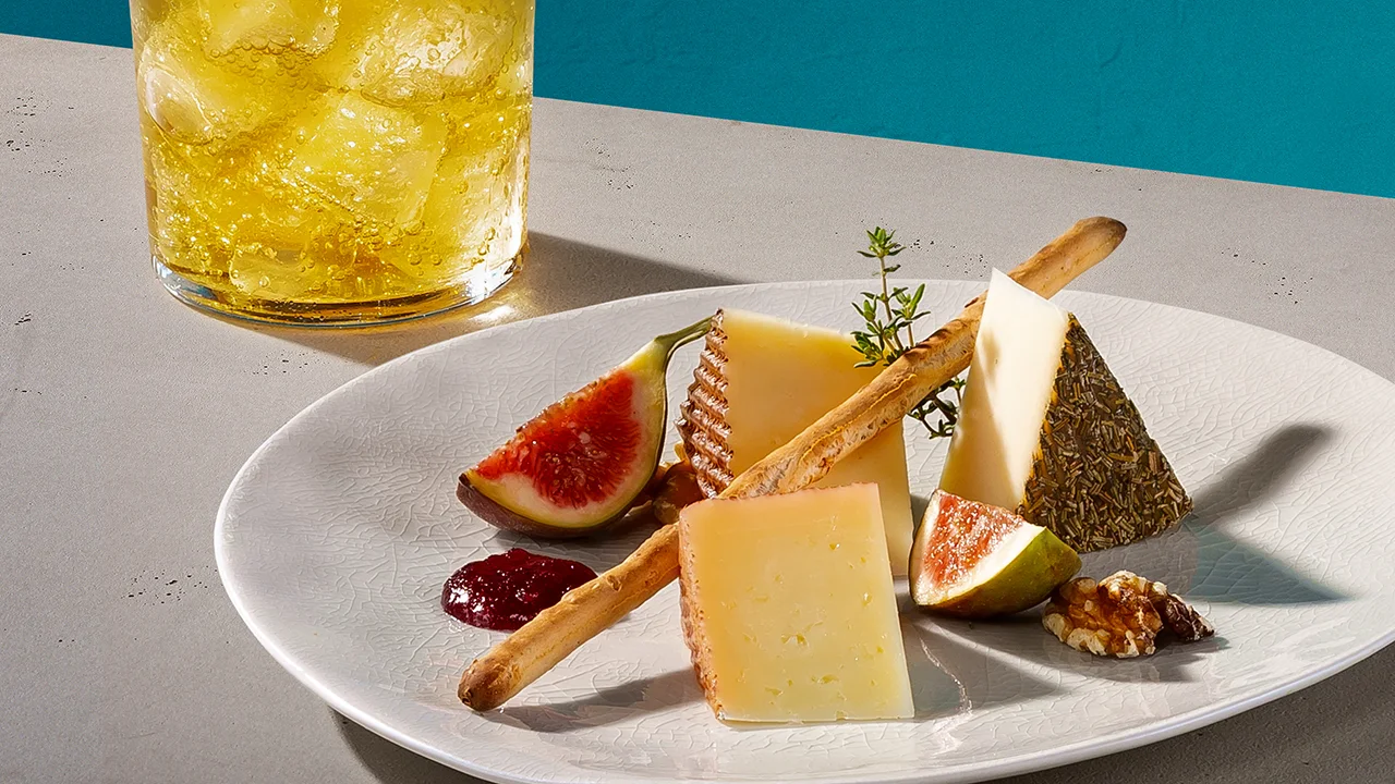 Ein gelber Whisky-Cocktail neben einem Teller mit Manchego und Feigensenf.