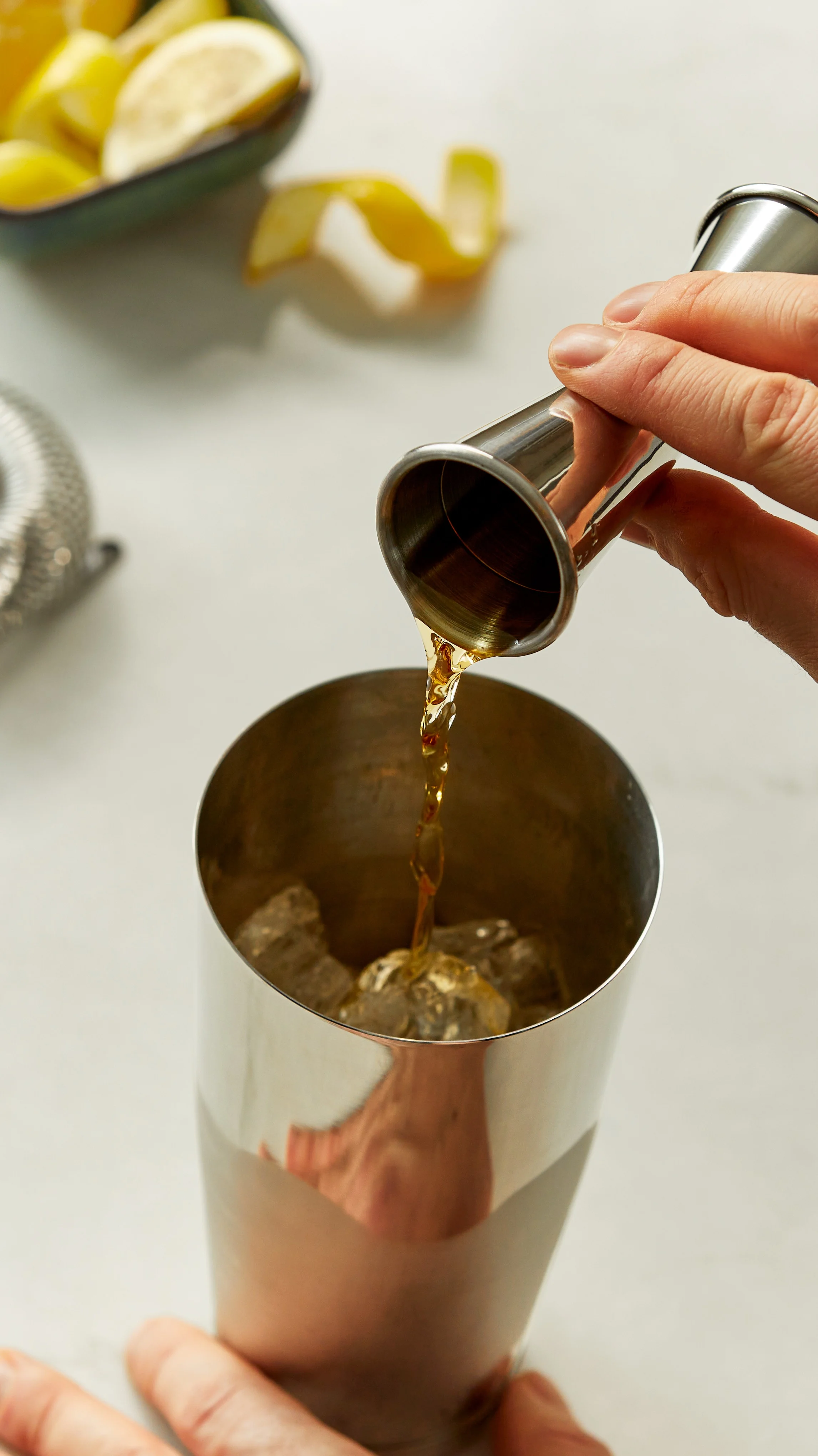Whisky wird mit einem Jigger in einen Cocktailshaker gegossen