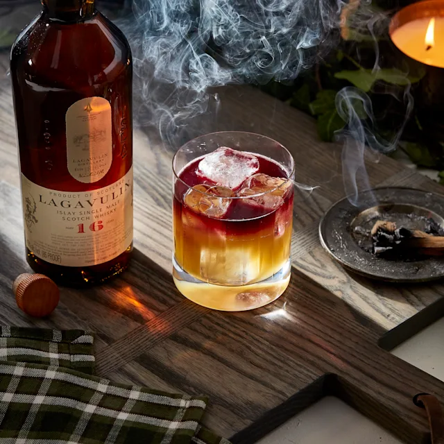 A lowball cocktail sits next to a bottle of Lagavulin 16 year old whisky