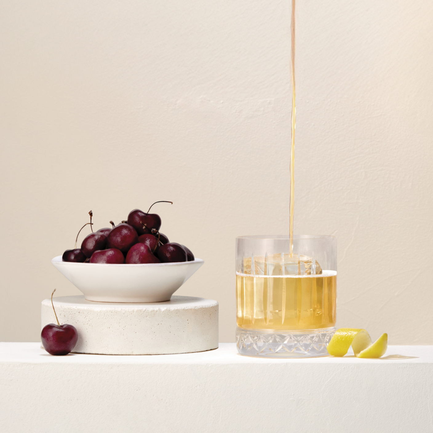 Whisky being poured into a glass next to a bowl of cherries