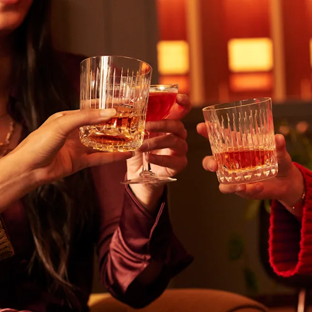 Three women hold glasses together in a 'cheers' motion. They contain assorted whisky cocktails.