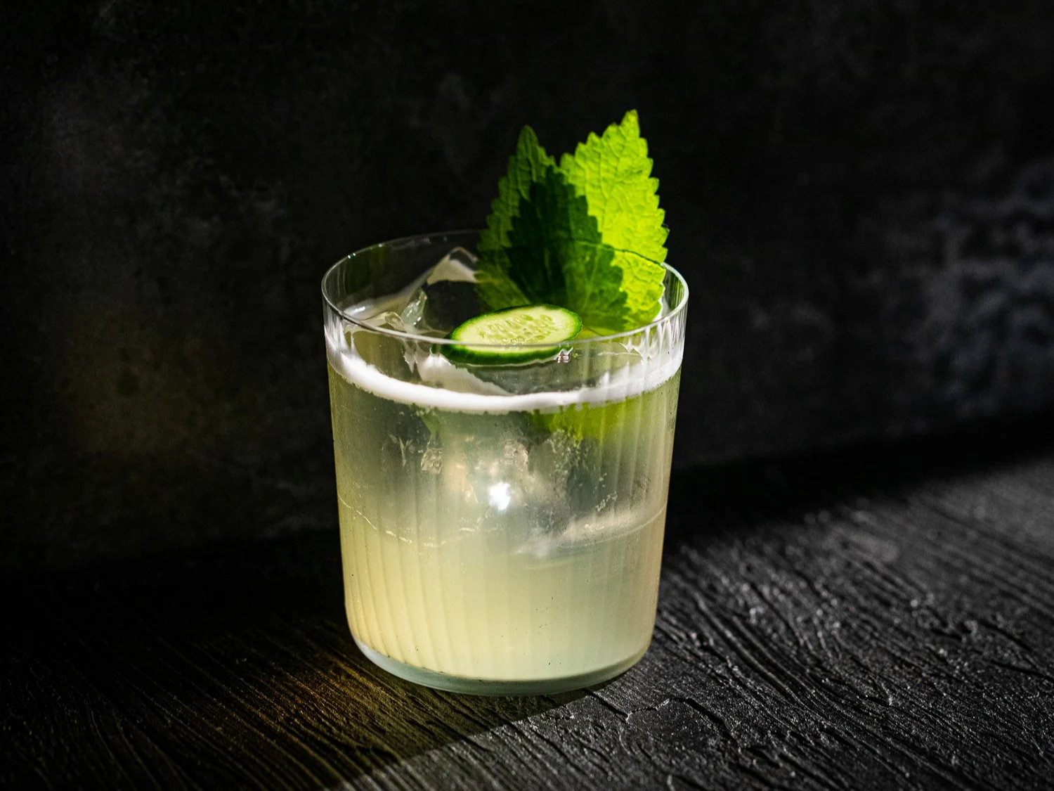 A light green cocktail in a rocks glass with a mint sprig garnish