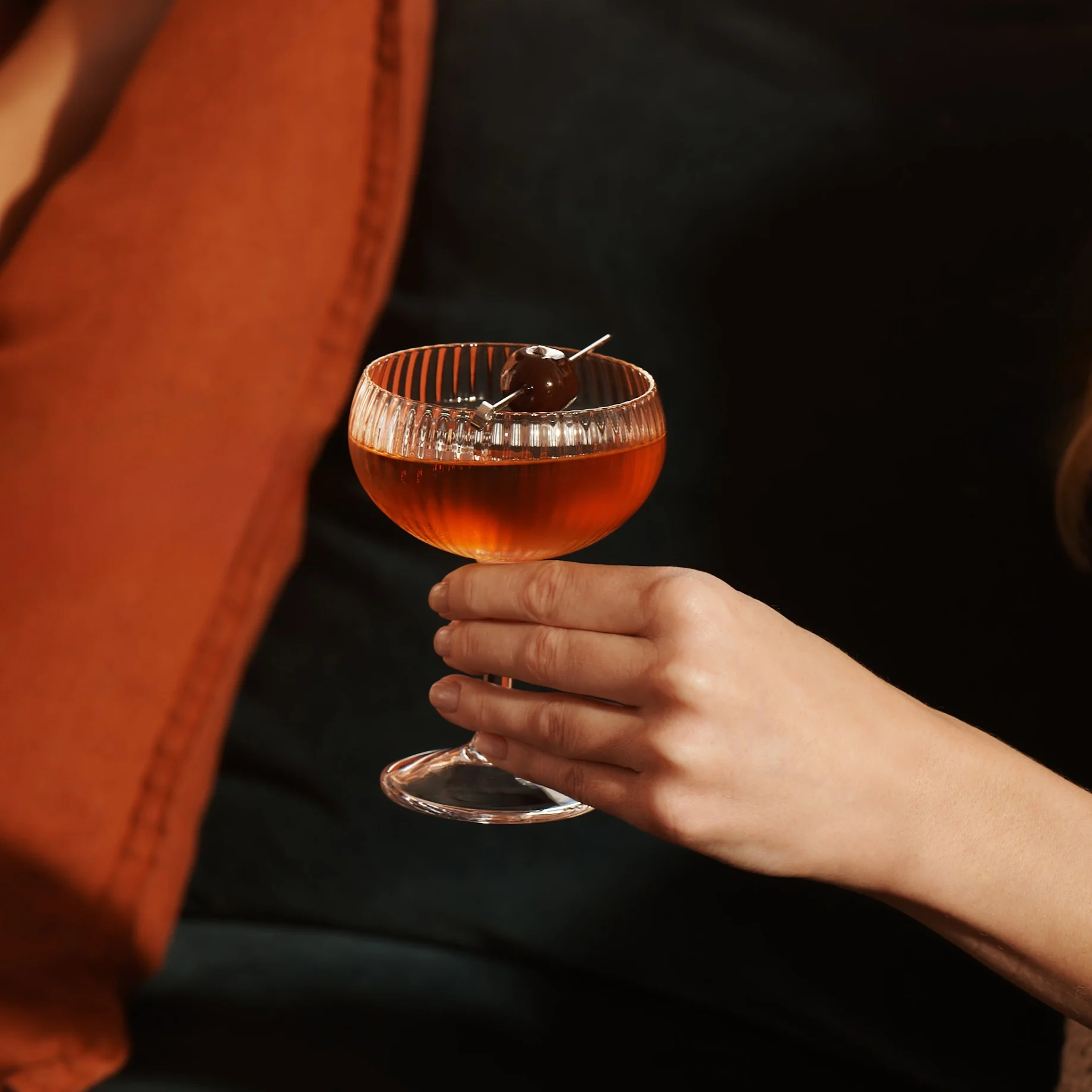Eine Frau sitzt auf einem Sofa und hält einen Whisky-Cocktail in einem Coupé-Glas