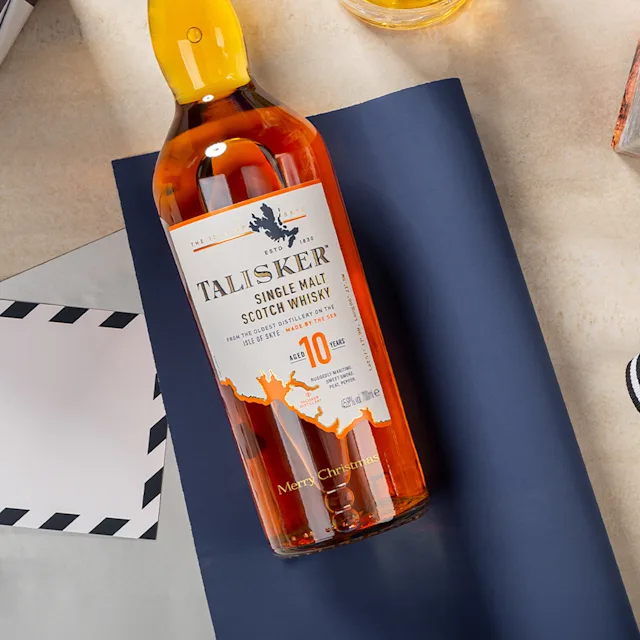 A bottle of Talisker 10 single malt whisky lies on a surface. It is engraved with the words 'Merry Christmas'.