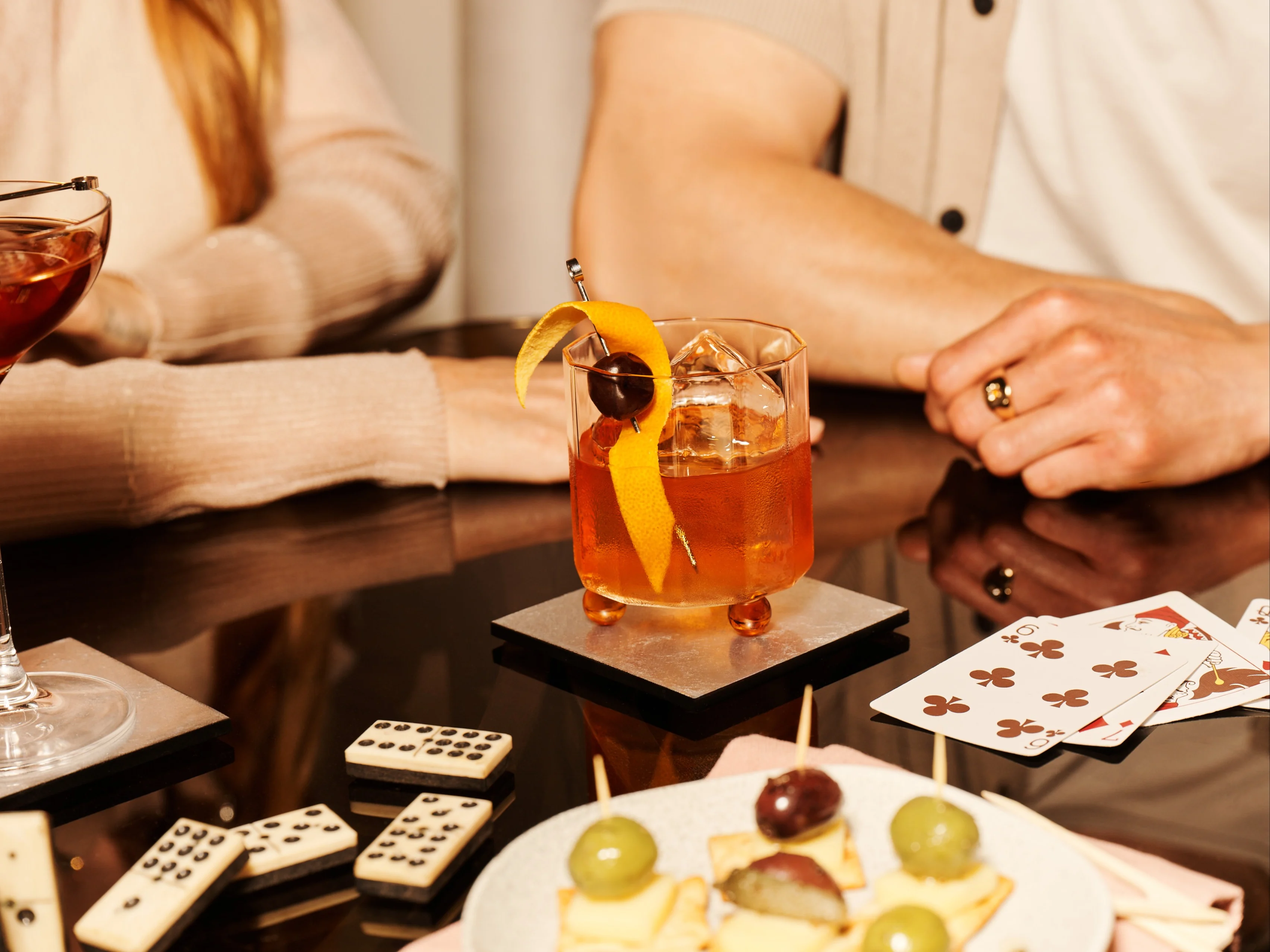 Zwei Personen stoßen mit Highball-Gläsern an, eines mit Cola und Eis, das andere mit einem Gold Rush-Cocktail mit Zitronengarnitur.