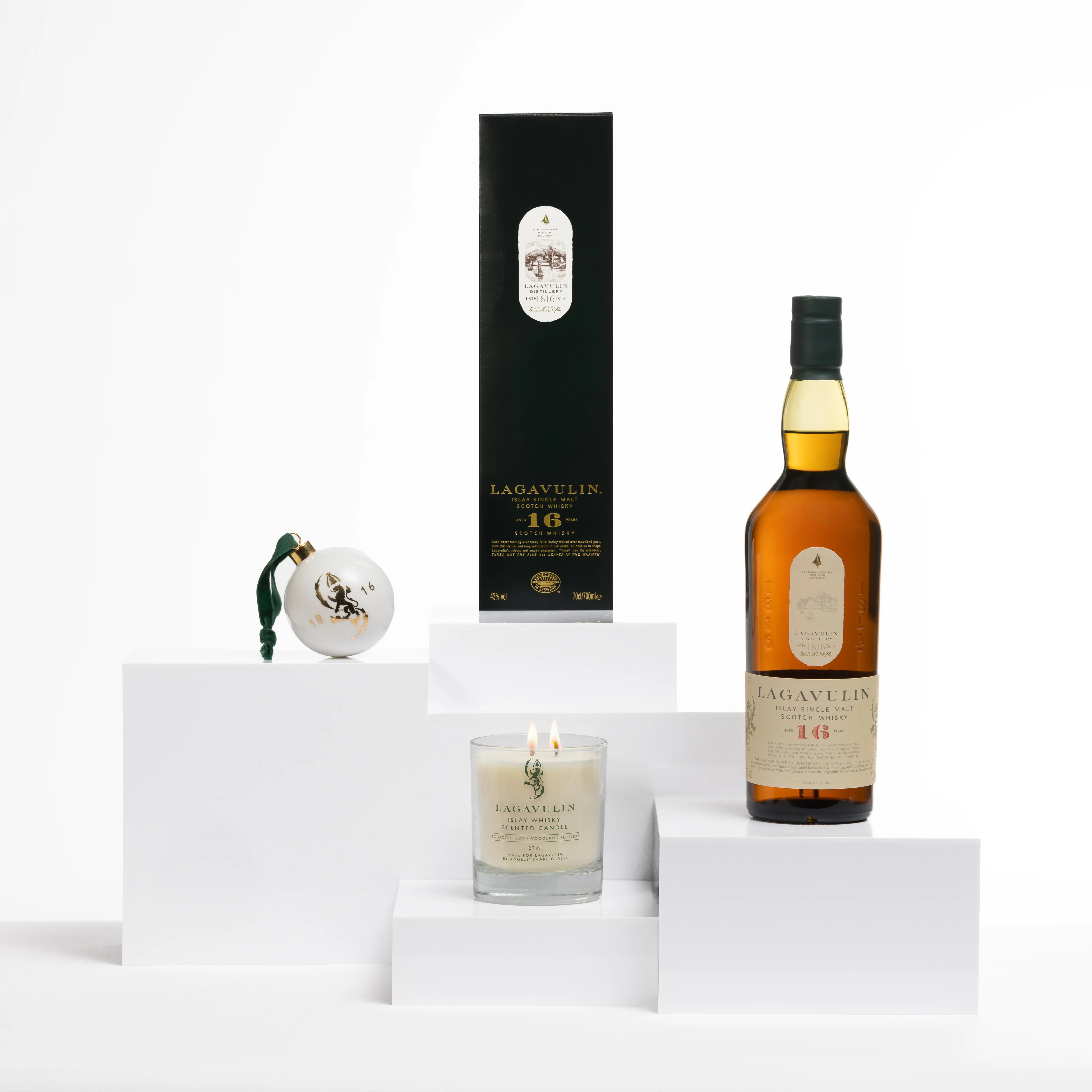 Lagavulin 16 Jahre Whisky mit passender Schachtel, einer festlichen Kugel und einer Doppel-Docht-Whisky-Duftkerze auf weißen Display-Blöcken.