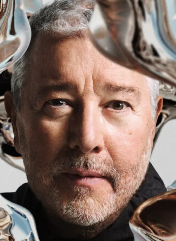 De ontwerper Philippe Starck kijkt naar de camera, terwijl vloeibaar zilver rond zijn gezicht stroomt.