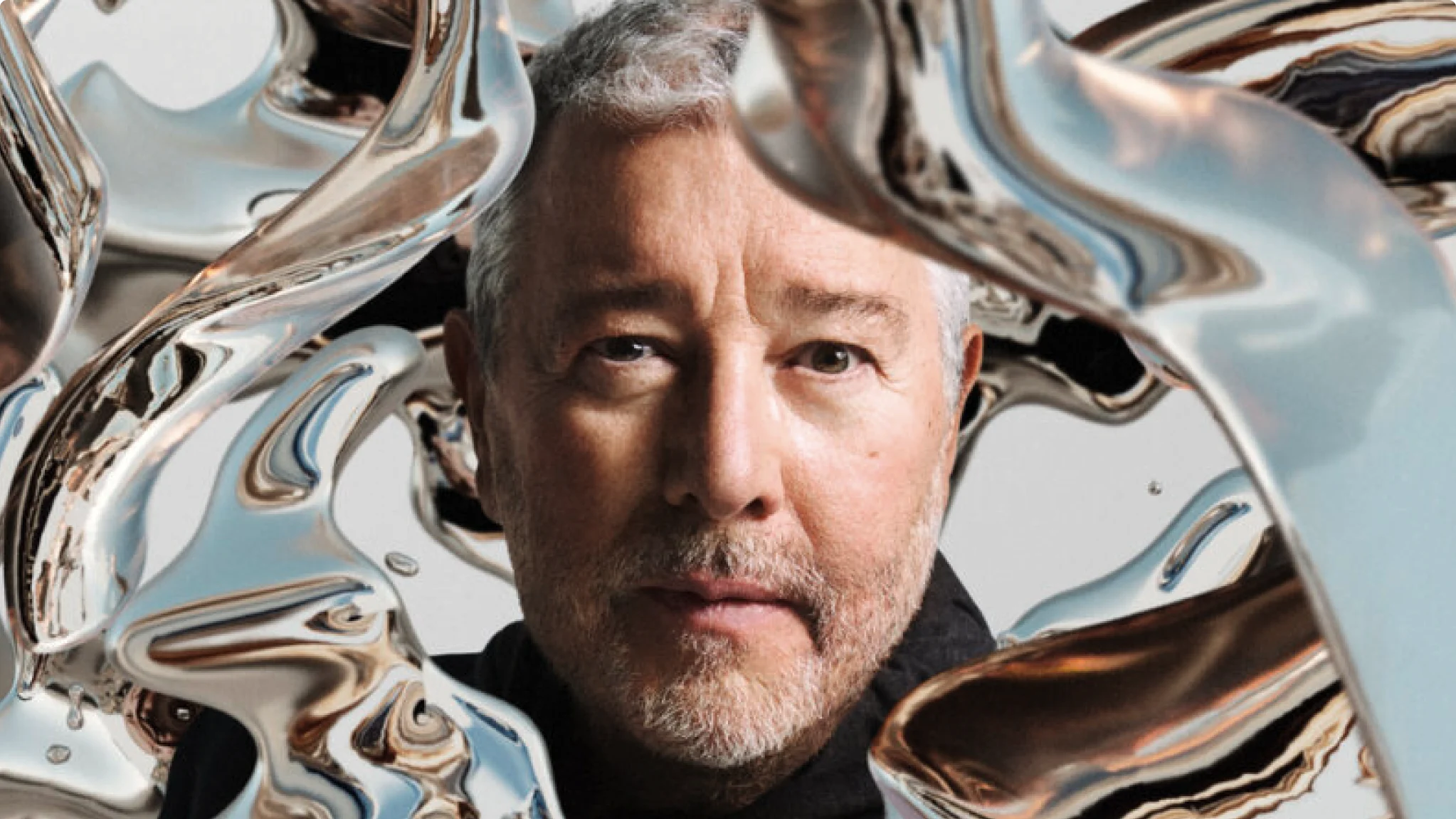 De ontwerper Philippe Starck kijkt naar de camera, terwijl vloeibaar zilver rond zijn gezicht stroomt.